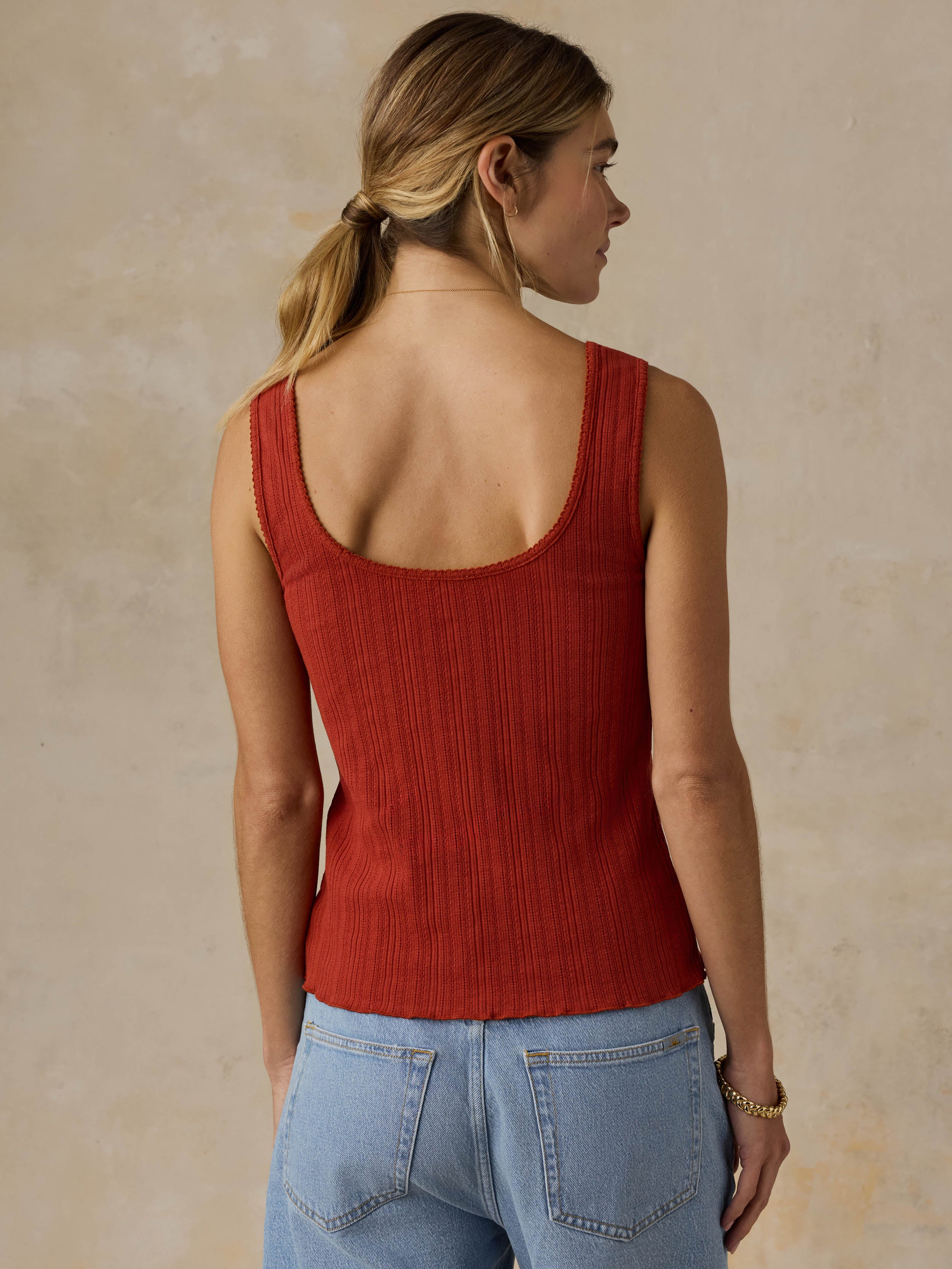 Woman wearing a red tank top and blue jeans against a beige background