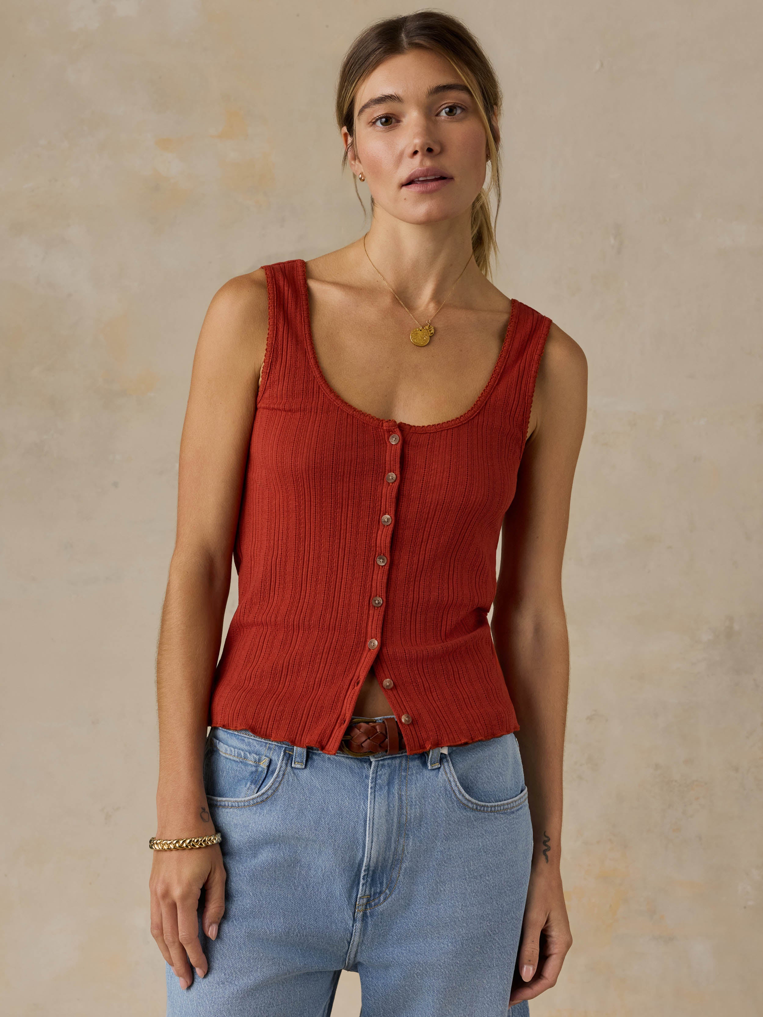 Woman wearing a red tank top and blue jeans against a beige background