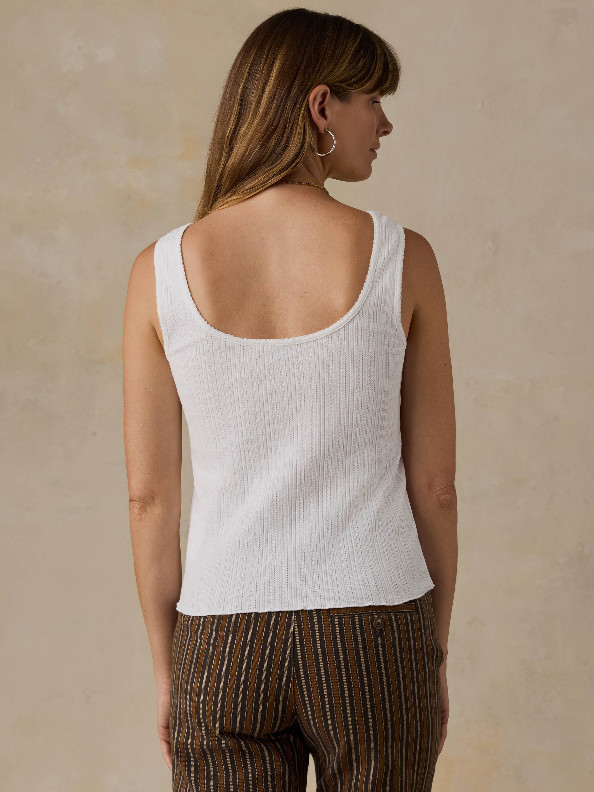 Woman wearing a white ribbed cami cardigan and brown striped pants against a beige background