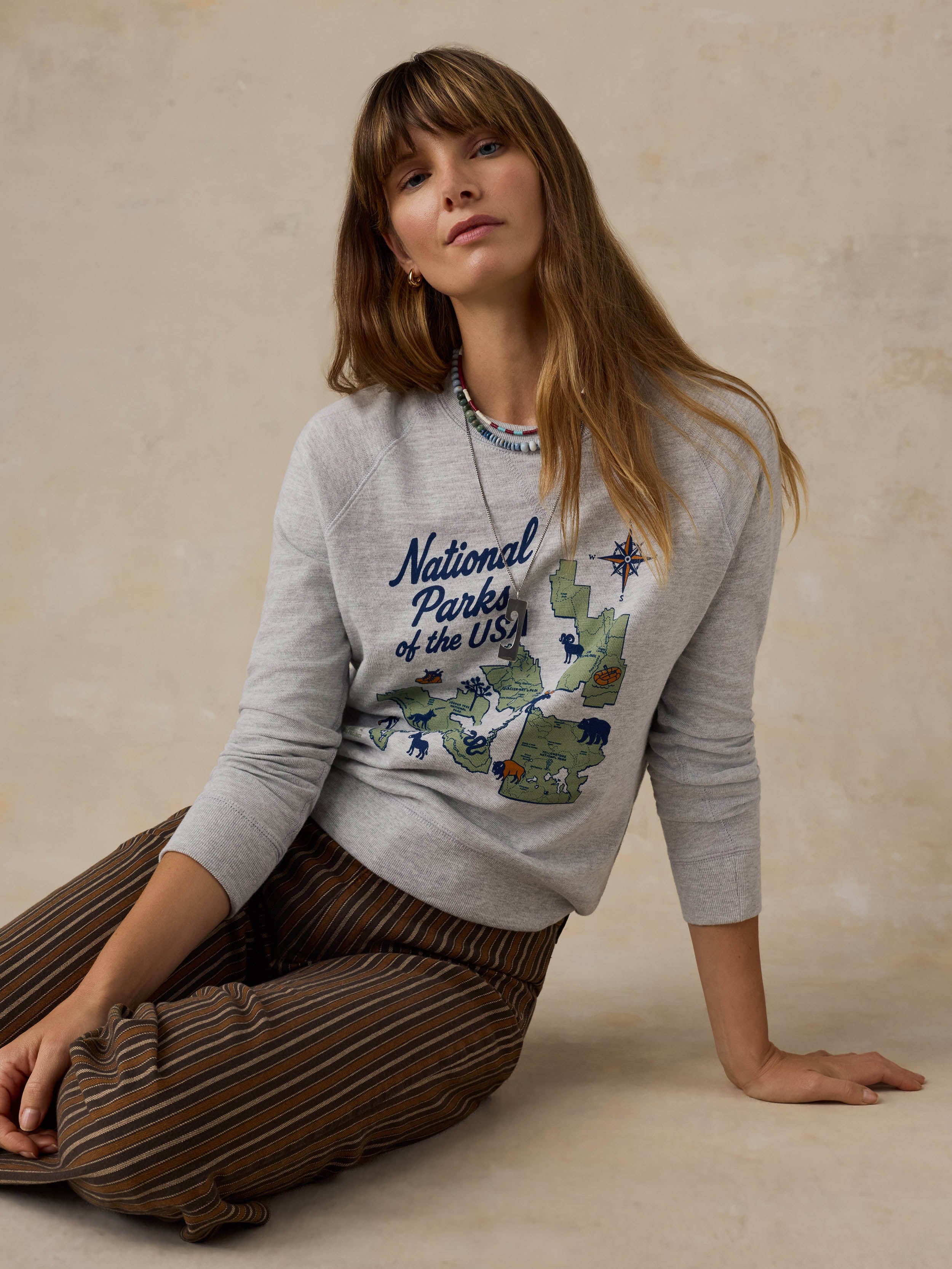 Woman wearing a grey crewneck with a National Parks graphic on the front against a beige background