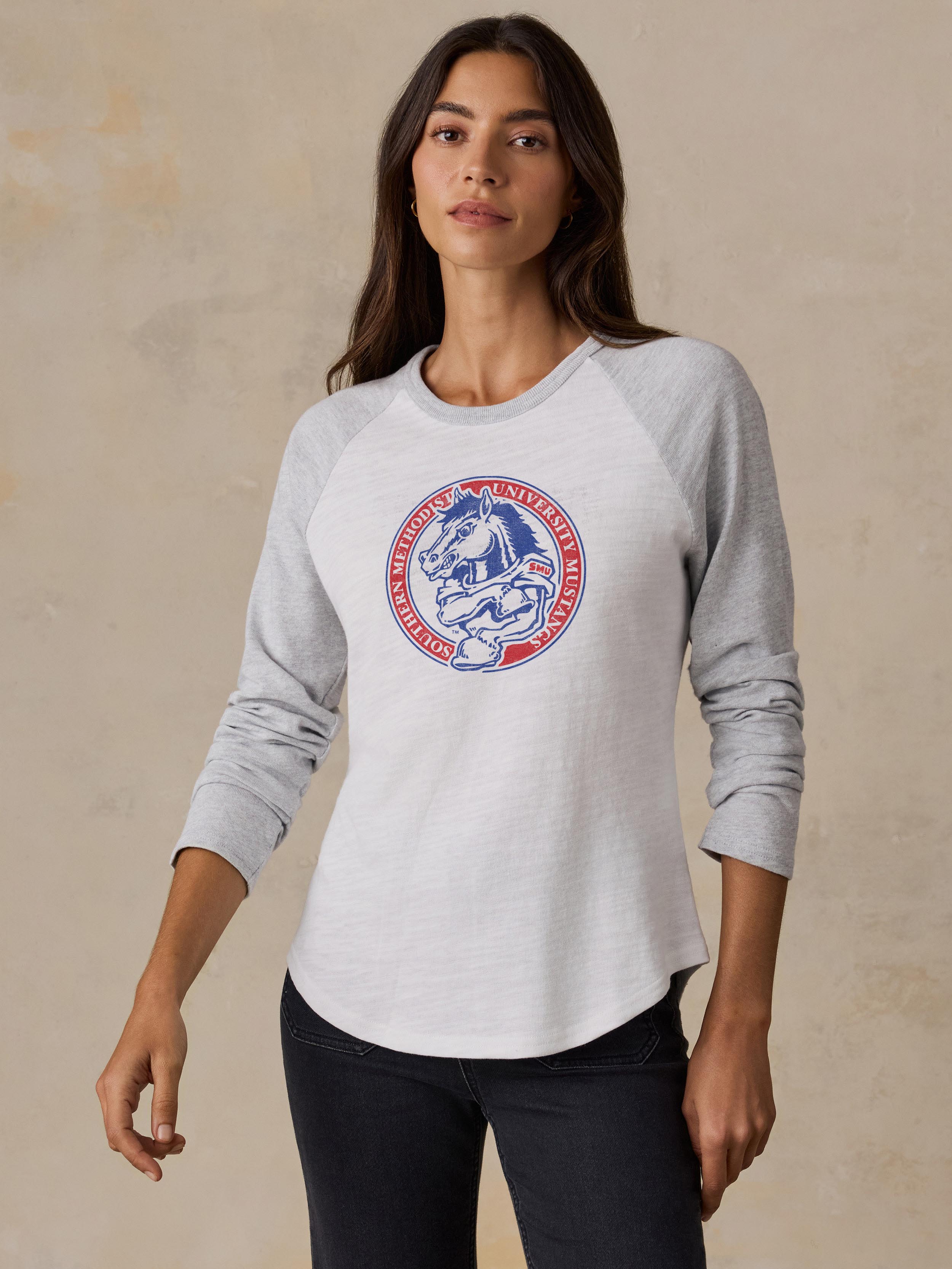 A woman wearing a white and grey SMU baseball tee and black jeans