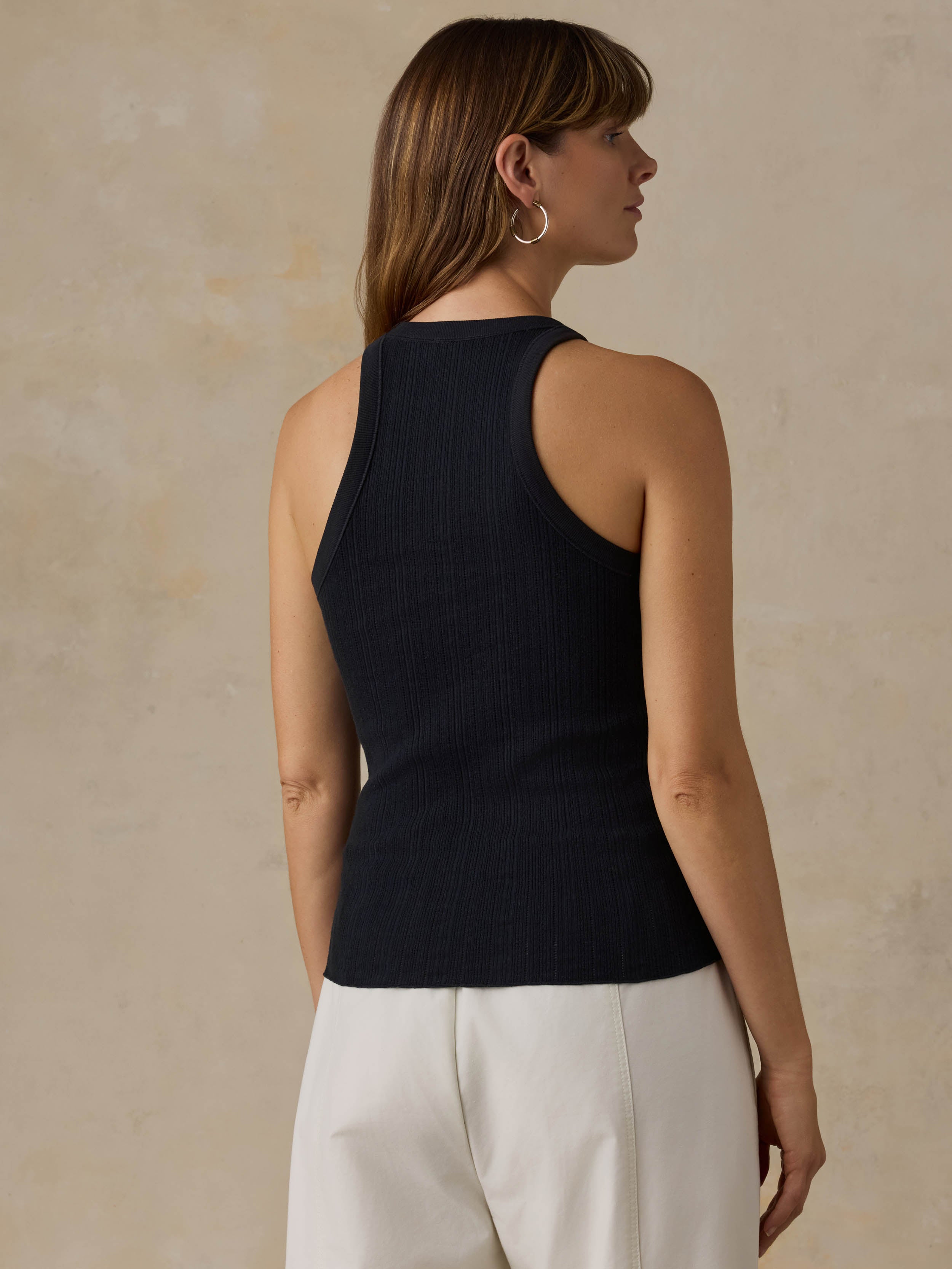 Woman wearing a black tank top and white pants against a beige background