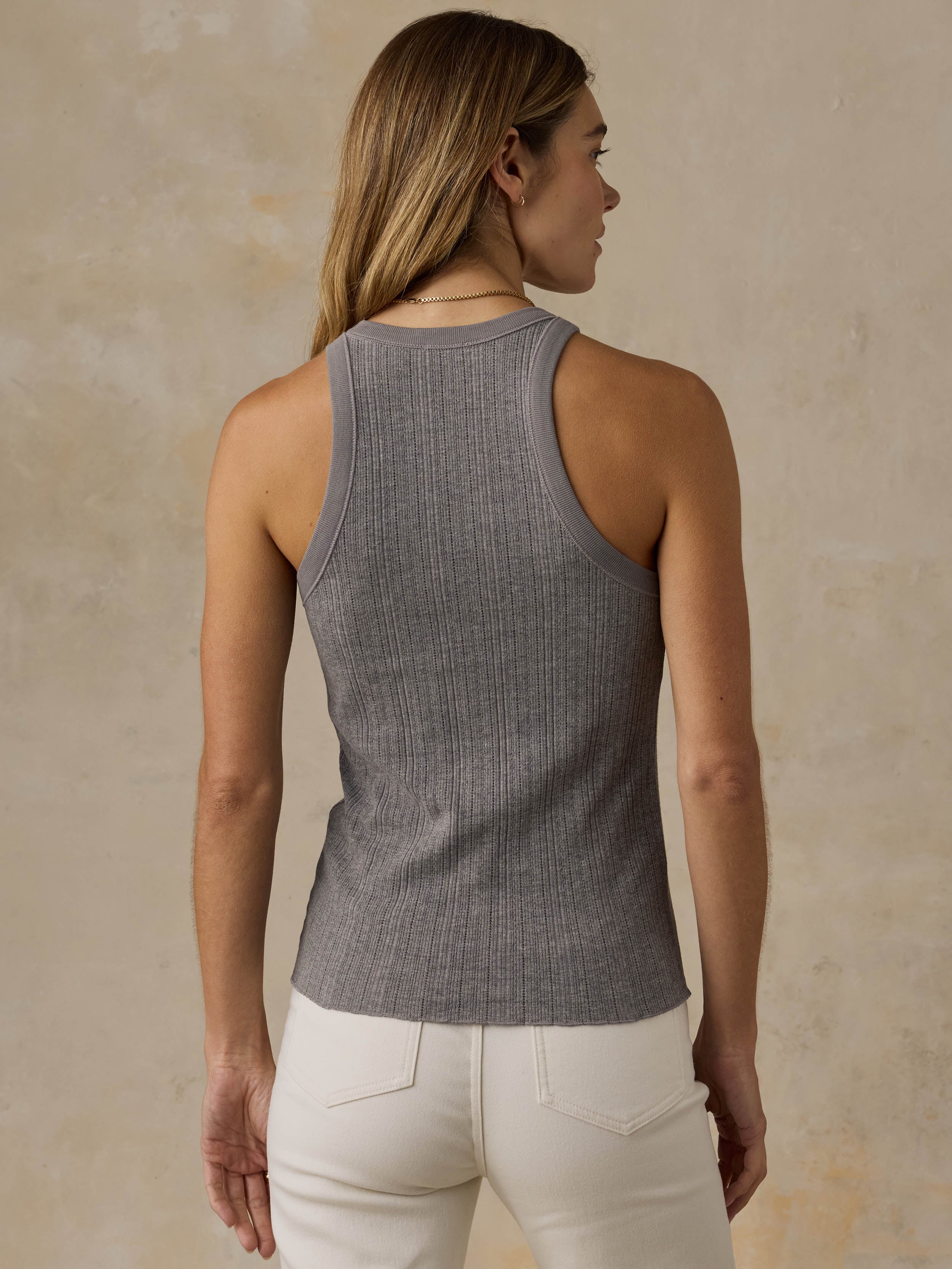 Woman wearing a grey tank top and white jeans against a beige background