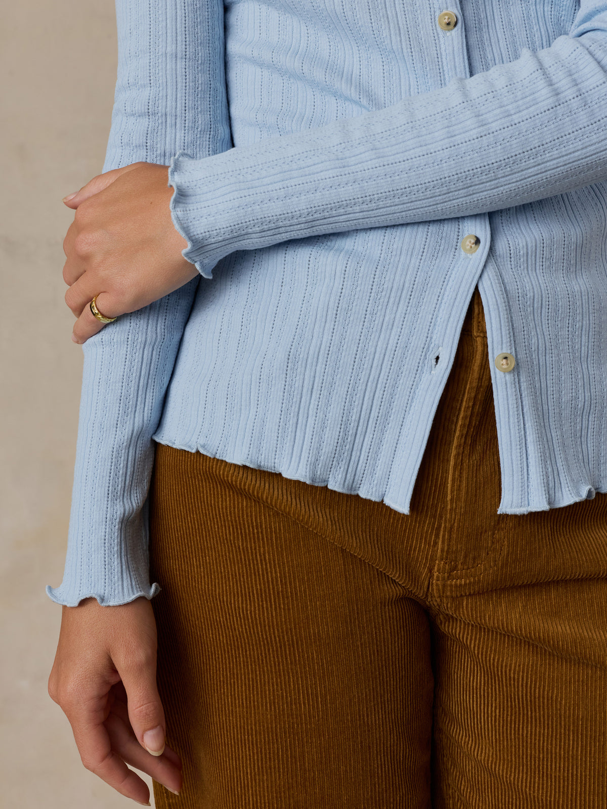 Close up of a woman wearing a light blue cardigan and brown corduroy pants, image 4 of 6