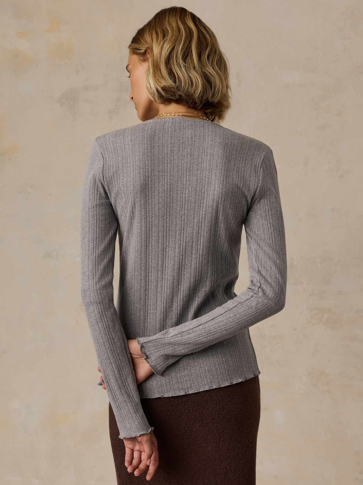 A woman viewed from behind wearing a grey cardigan and brown skirt, image 3 of 6