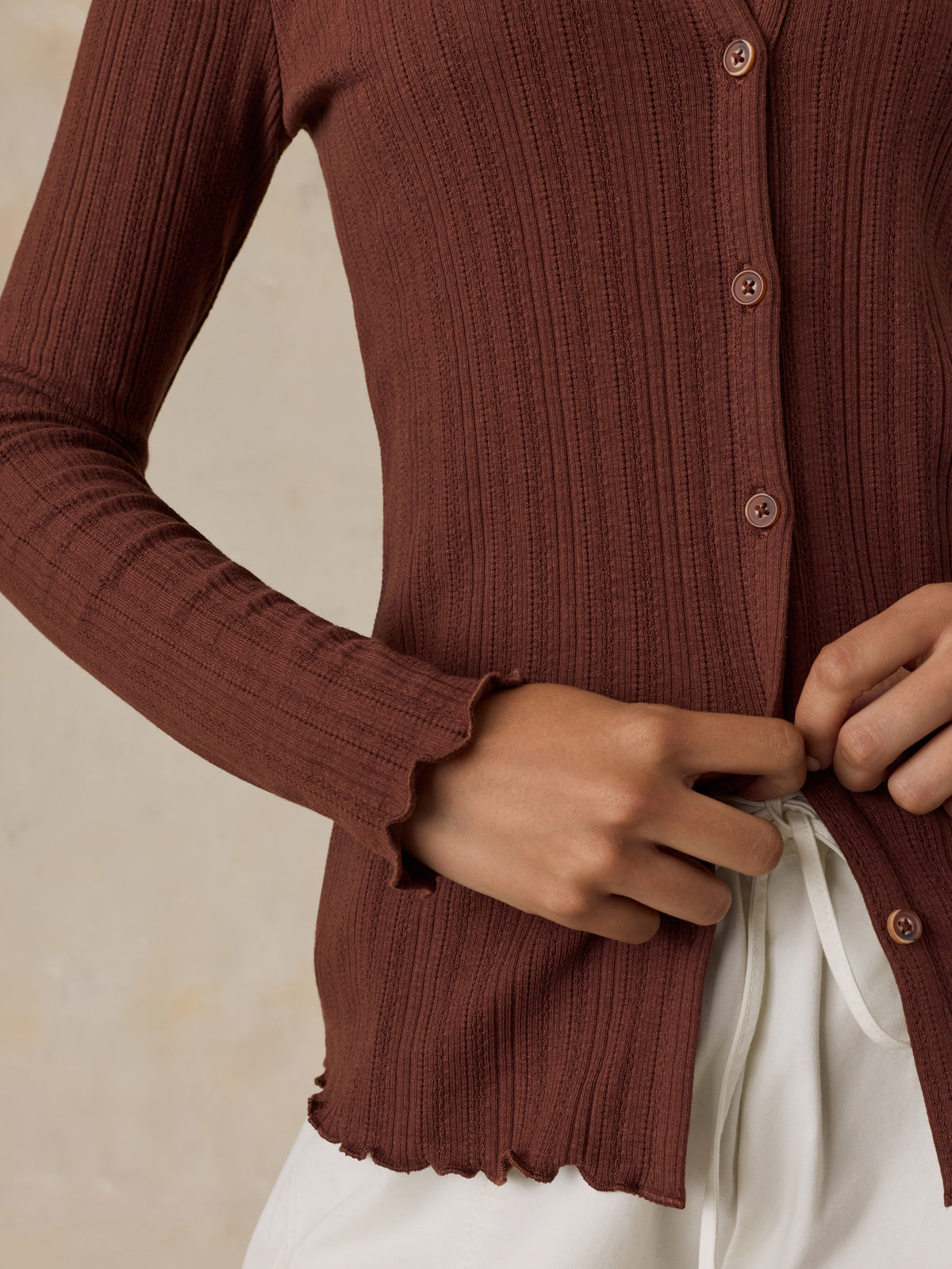 Close up of a woman wearing a brown cardigan and white pants, image 4 of 6