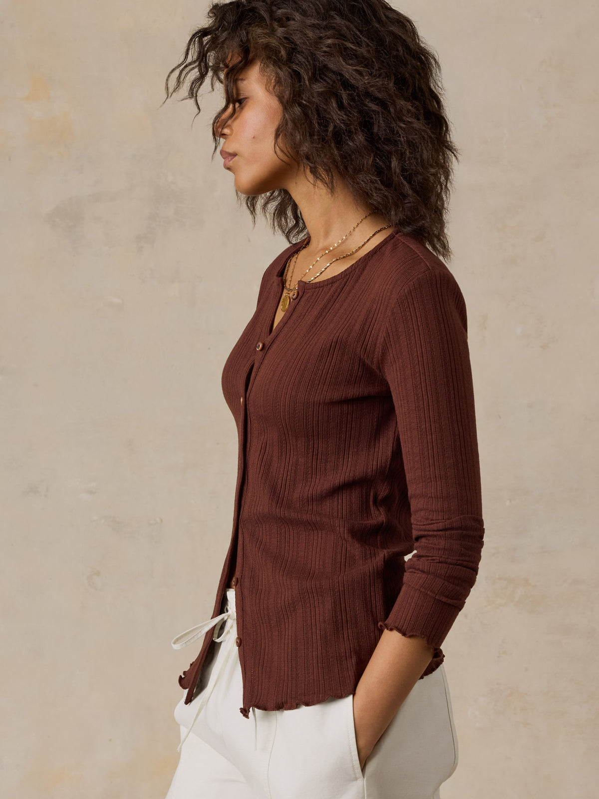 A woman wearing a brown knit cardigan and white pants, image 5 of 6