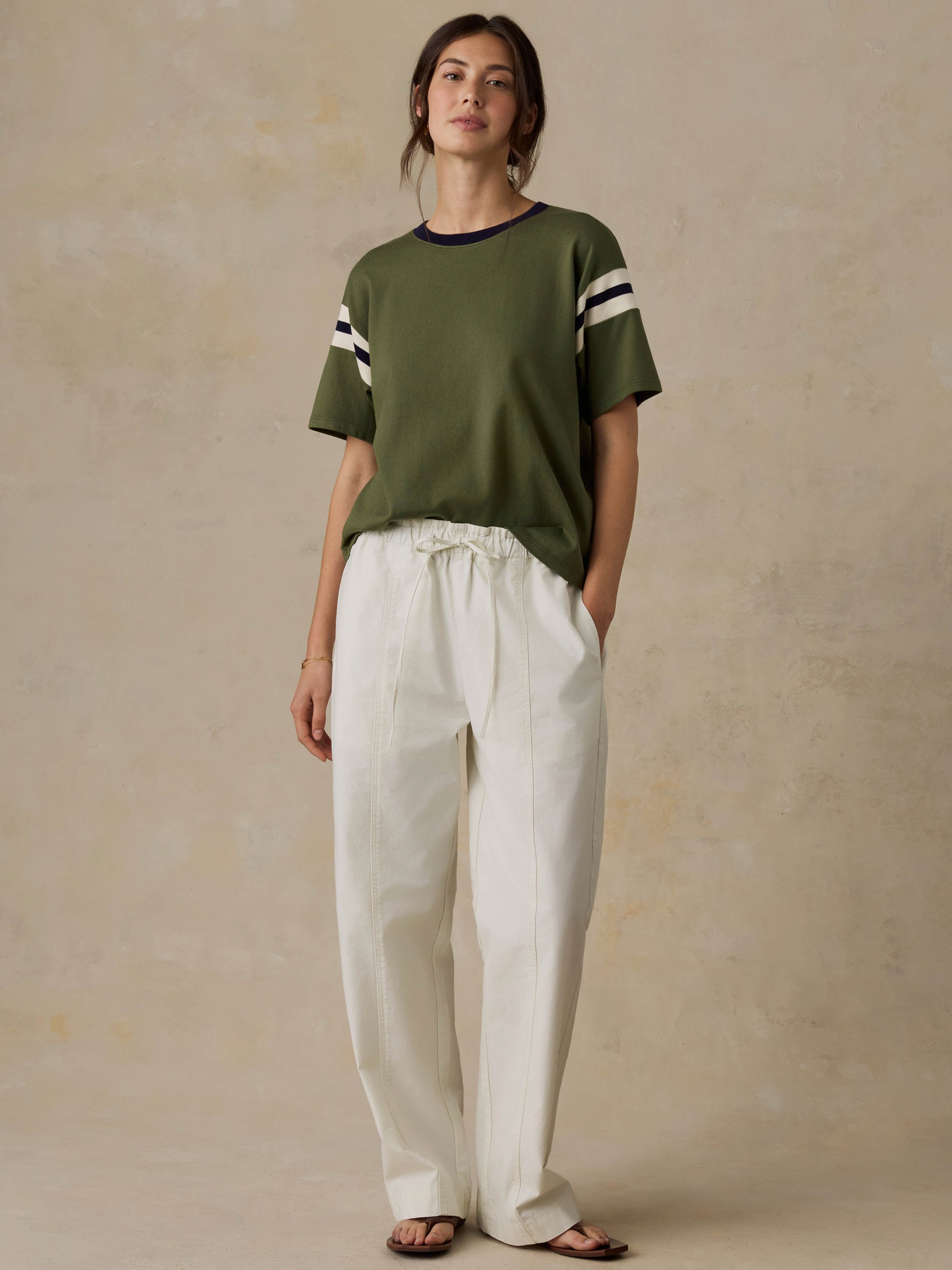 Woman wearing a green and white striped shirt with white pants against a beige background