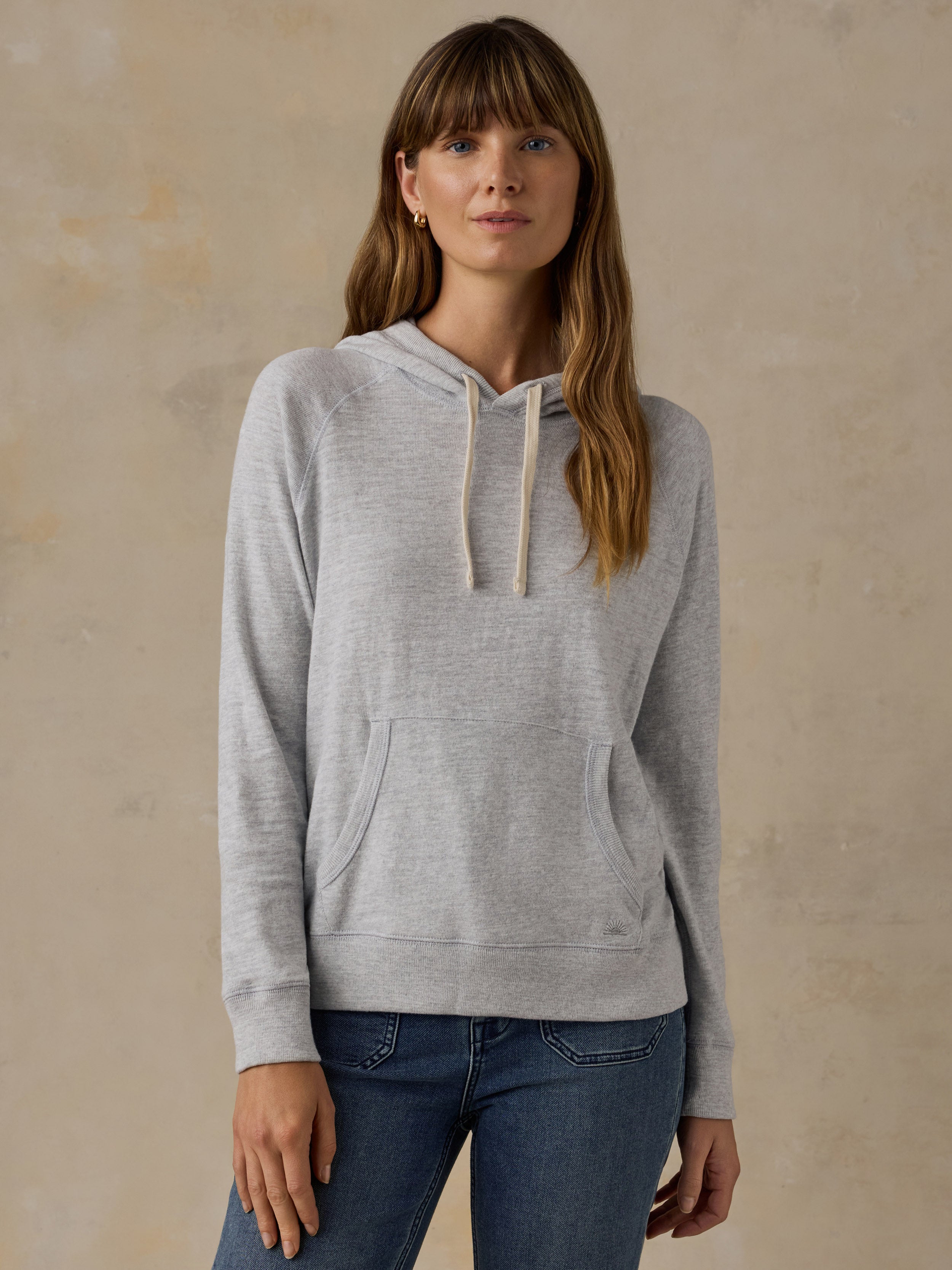 Woman wearing a grey sweatshirt and blue jeans against a beige background