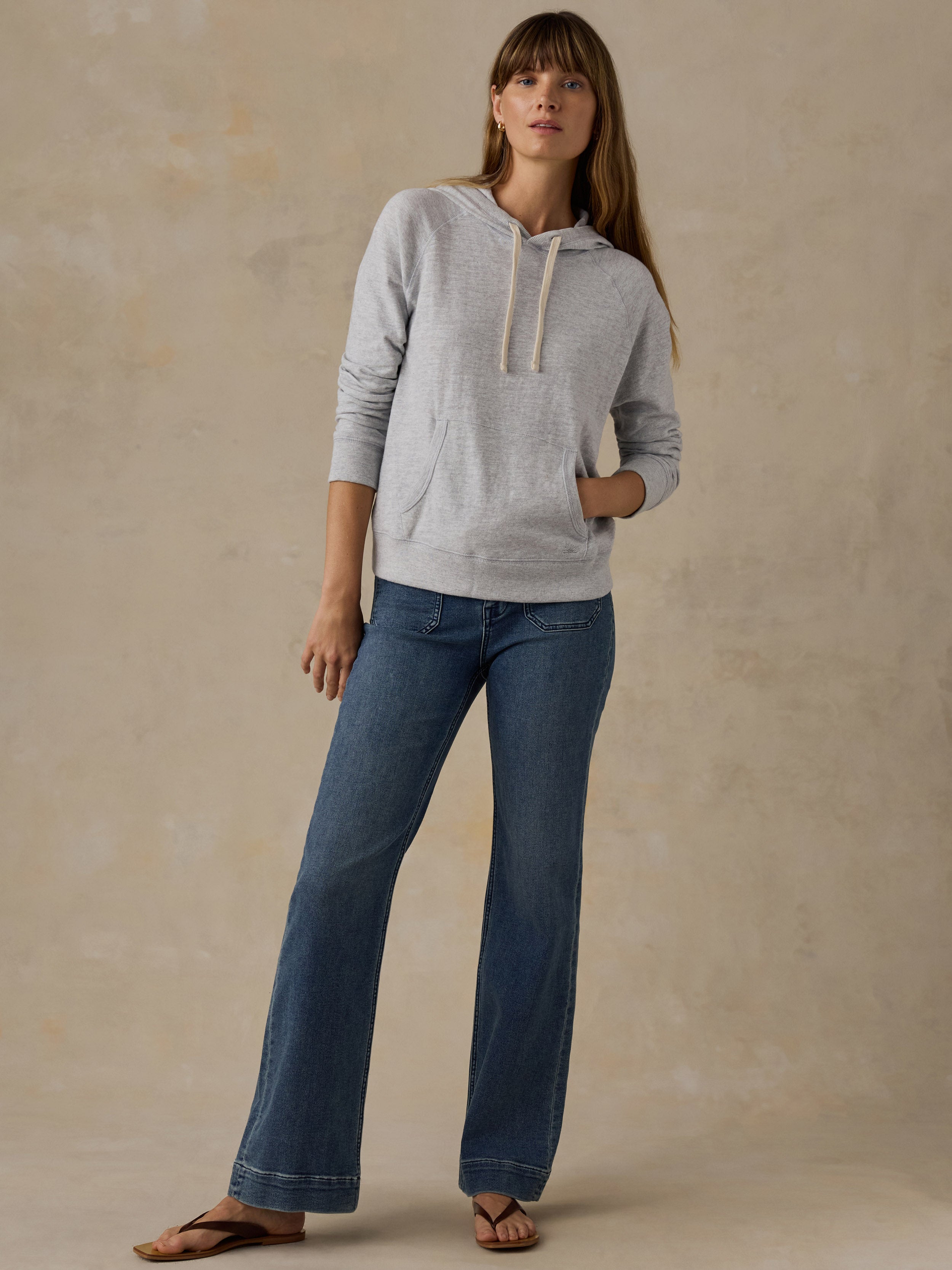 Woman wearing a grey sweatshirt and blue jeans against a beige background