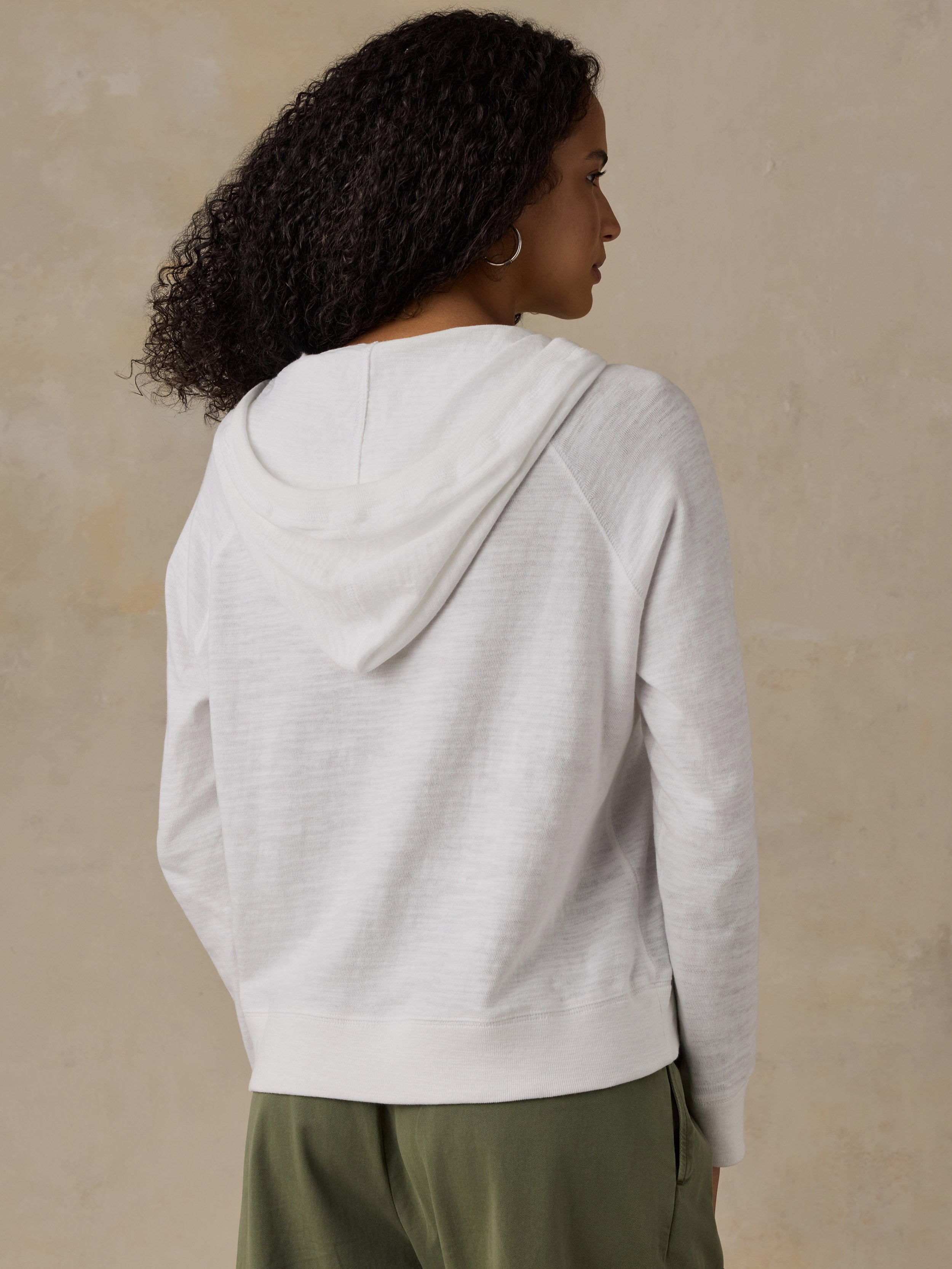 Woman wearing a white hoodie and olive green pants against a beige background