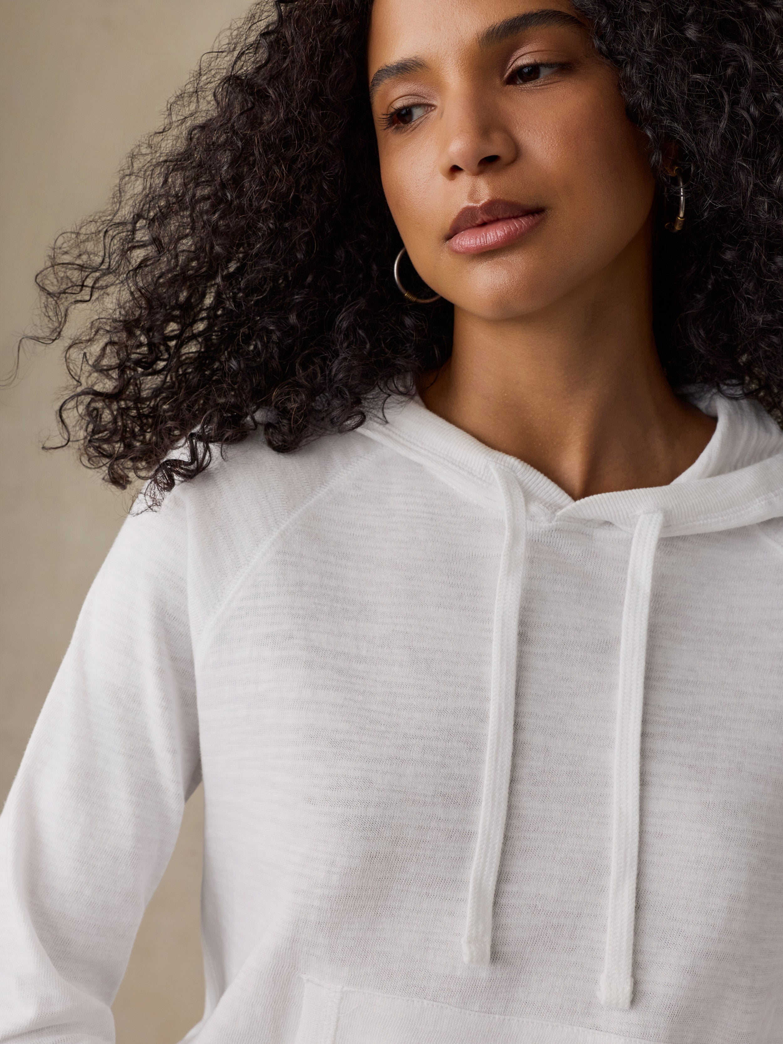 Close-up of a woman wearing a white hoodie against a beige background