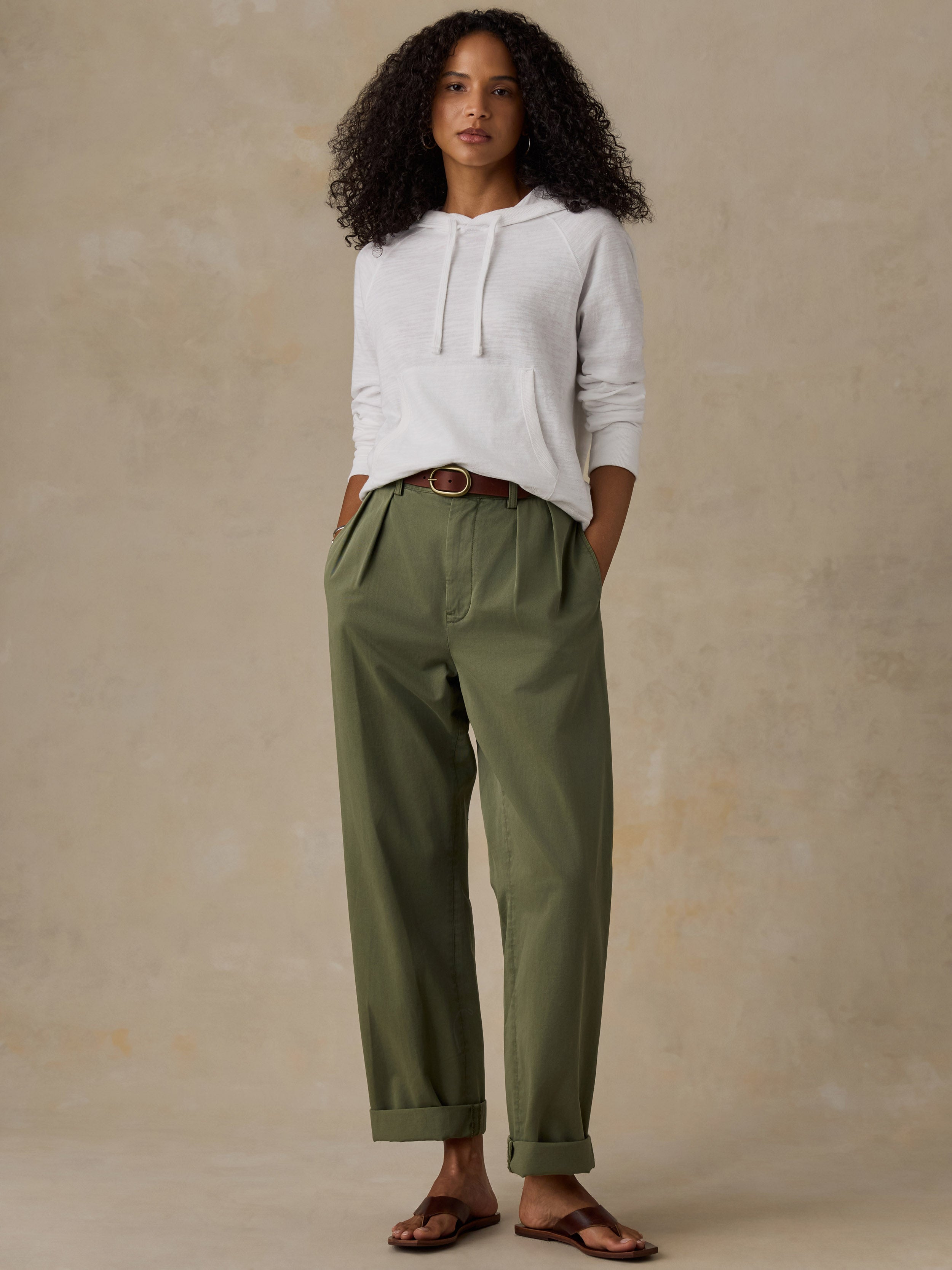 Woman wearing a white hoodie and olive green pants against a beige background