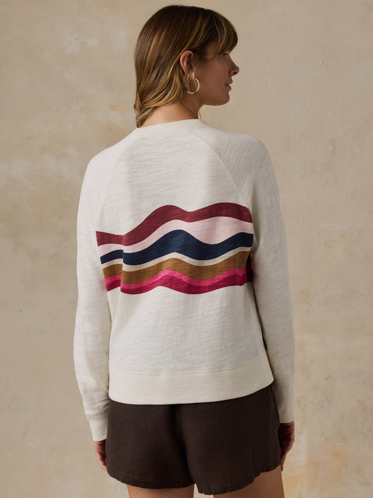 Woman wearing a white and multicolor graphic crewneck with brown linen shorts against a beige background, image 3 of 6