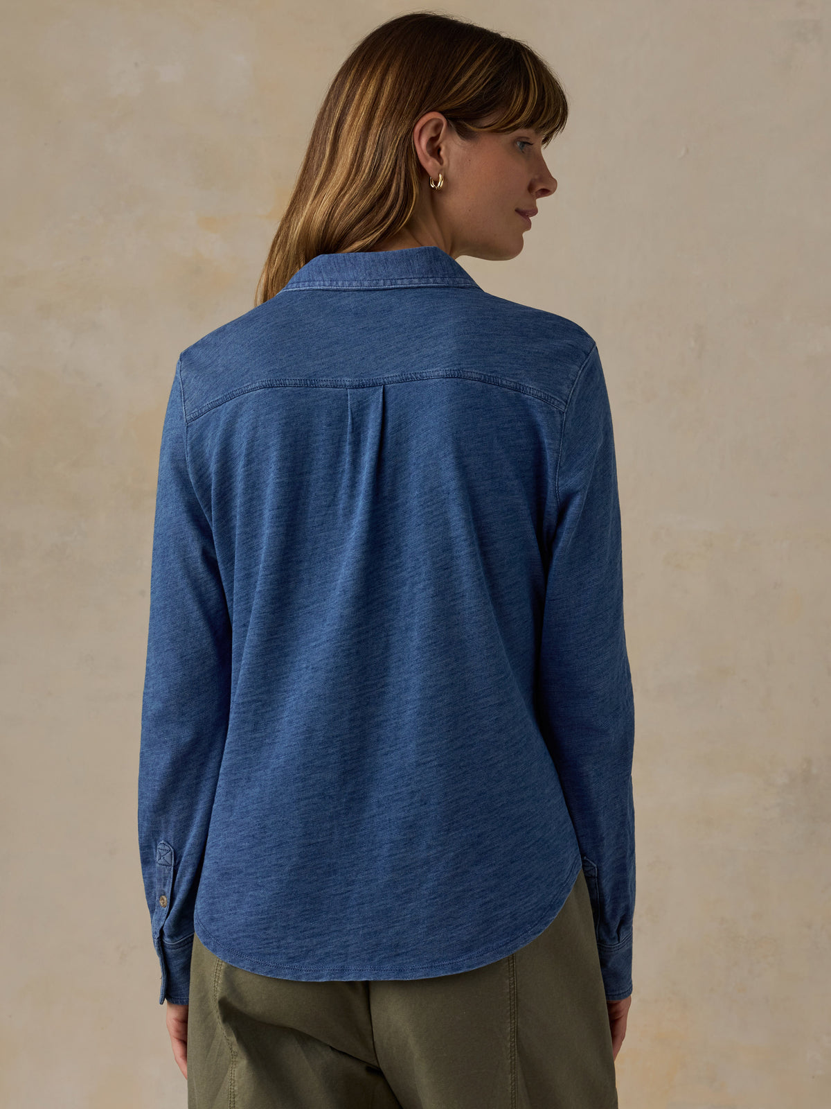 Woman wearing a blue button down shirt and olive green pants against a beige background, image 3 of 6