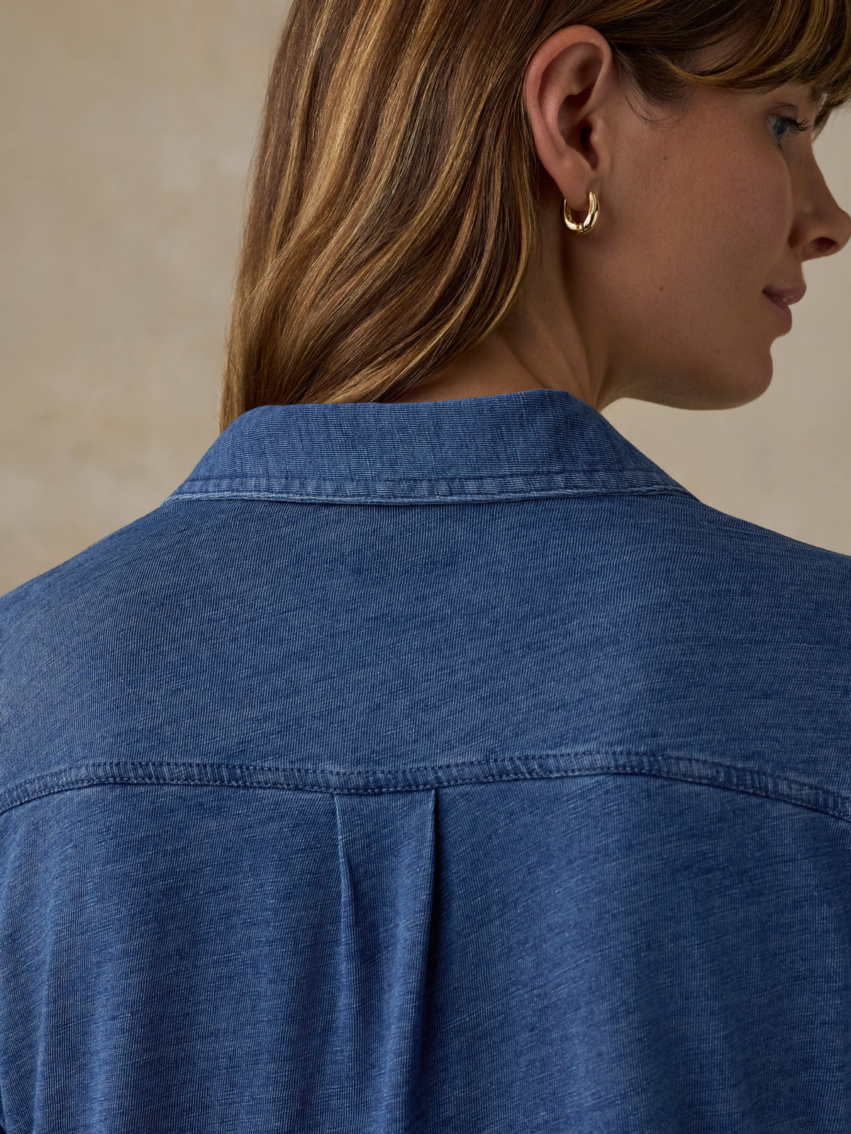 Woman wearing a blue button down shirt against a beige background, image 6 of 6