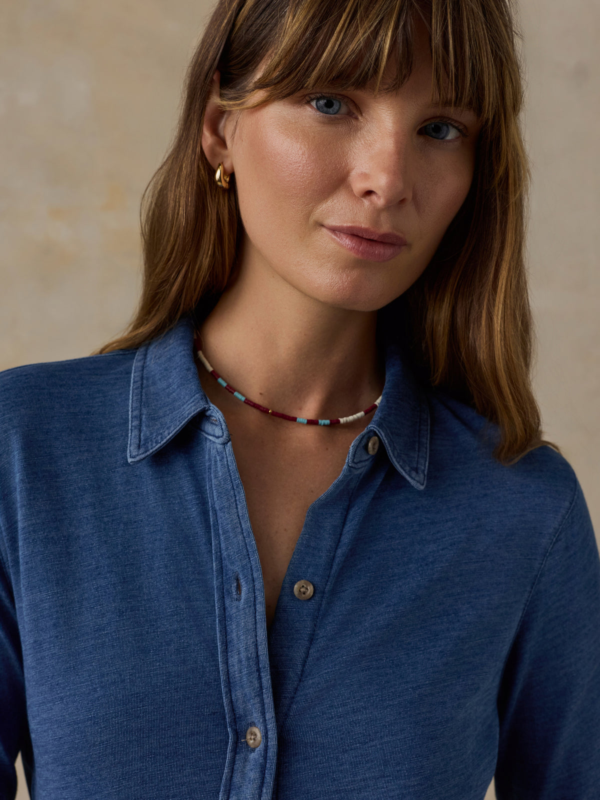 Woman wearing a blue button down shirt against a beige background, image 2 of 6