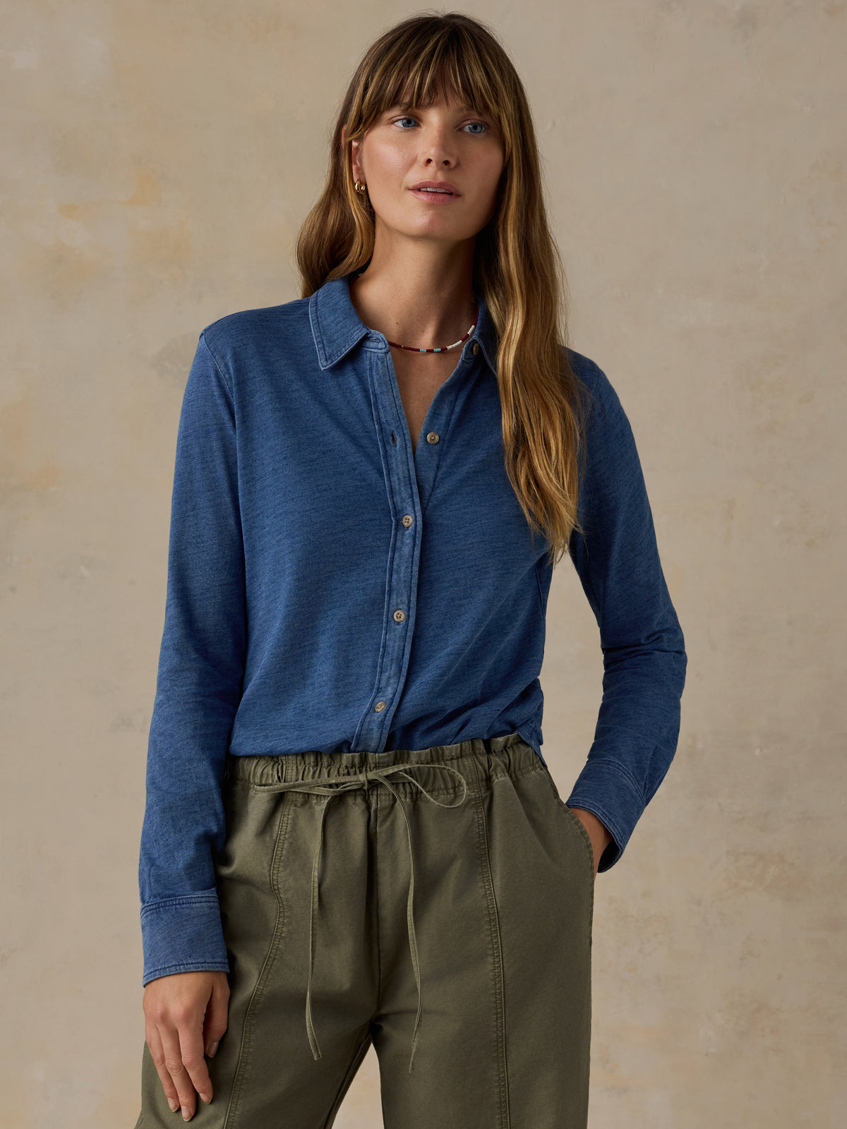 Woman wearing a blue button down shirt and olive green pants against a beige background, image 1 of 6