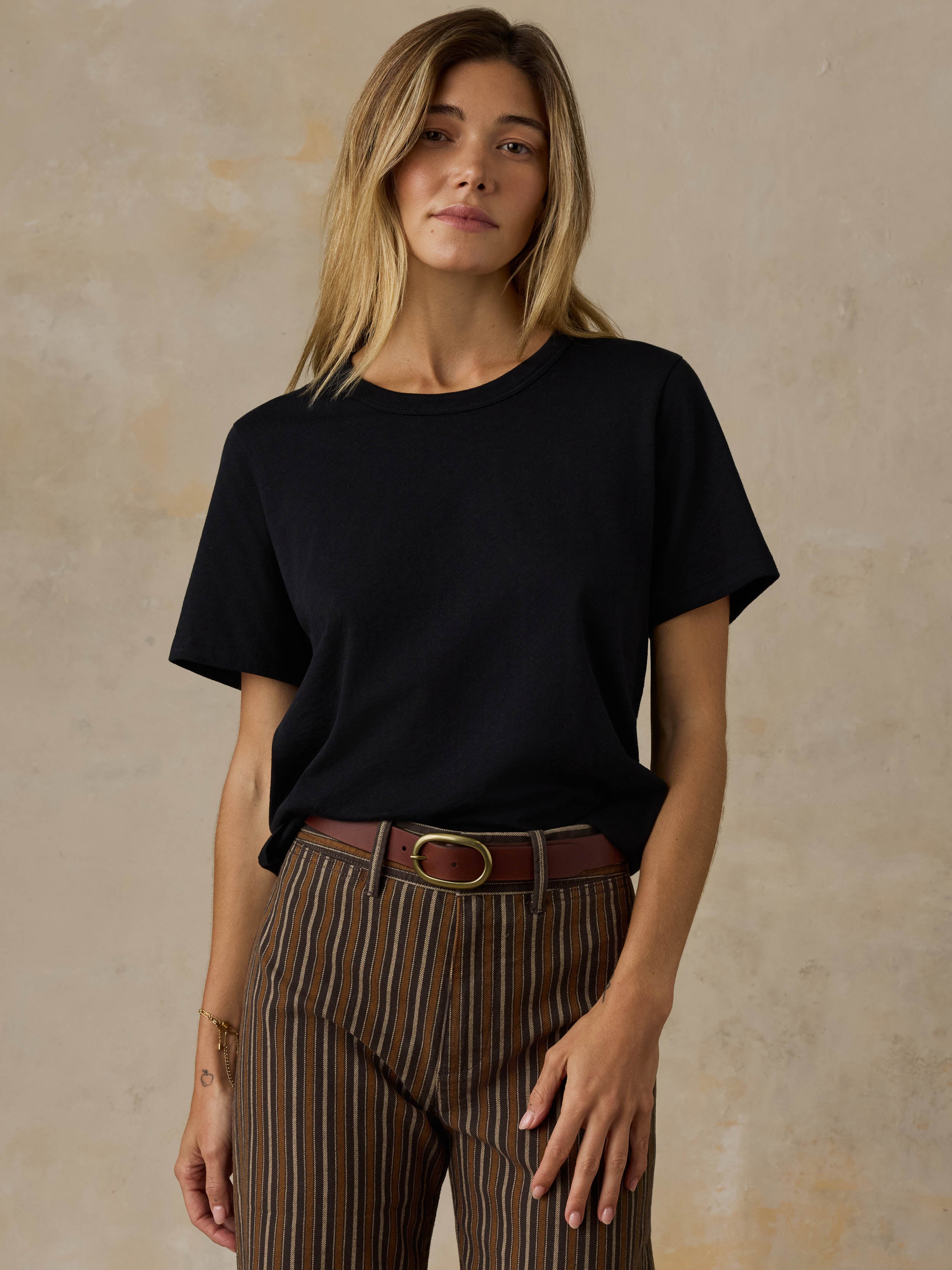 Woman wearing a black t-shirt and striped pants against a beige background