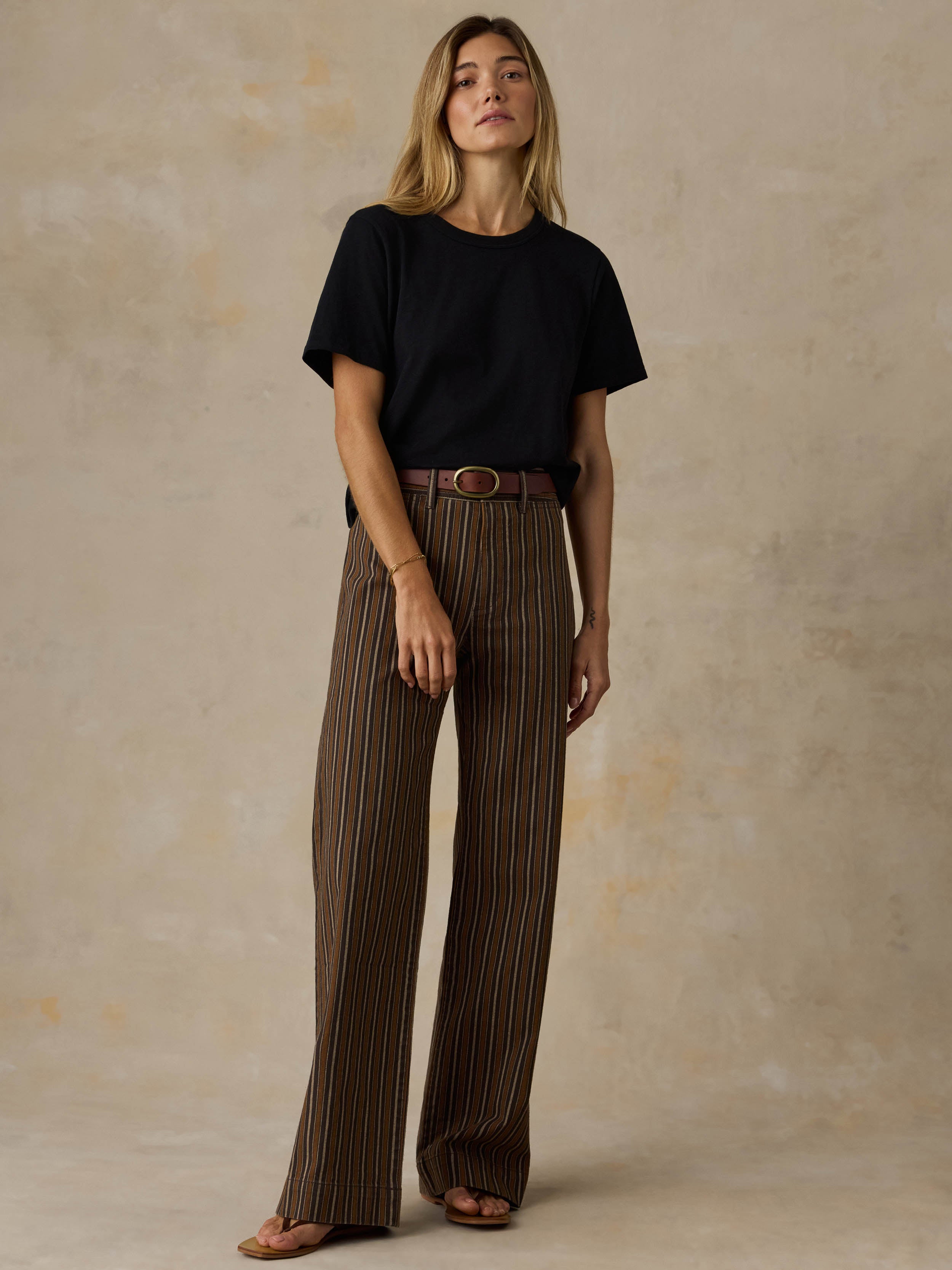 Woman wearing a black t-shirt and striped pants against a beige background