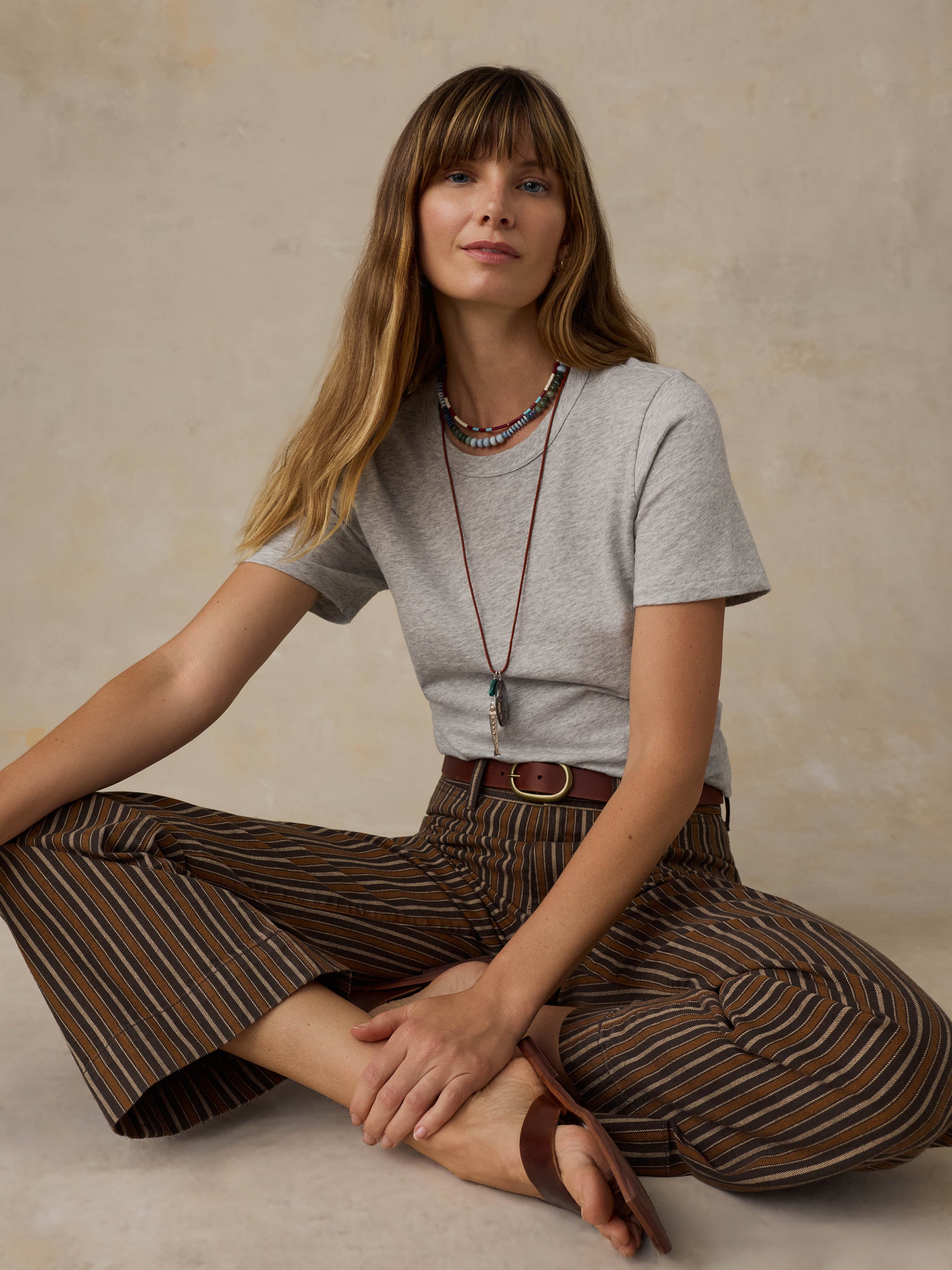 A woman wearing a grey t-shirt and striped pants against a beige background