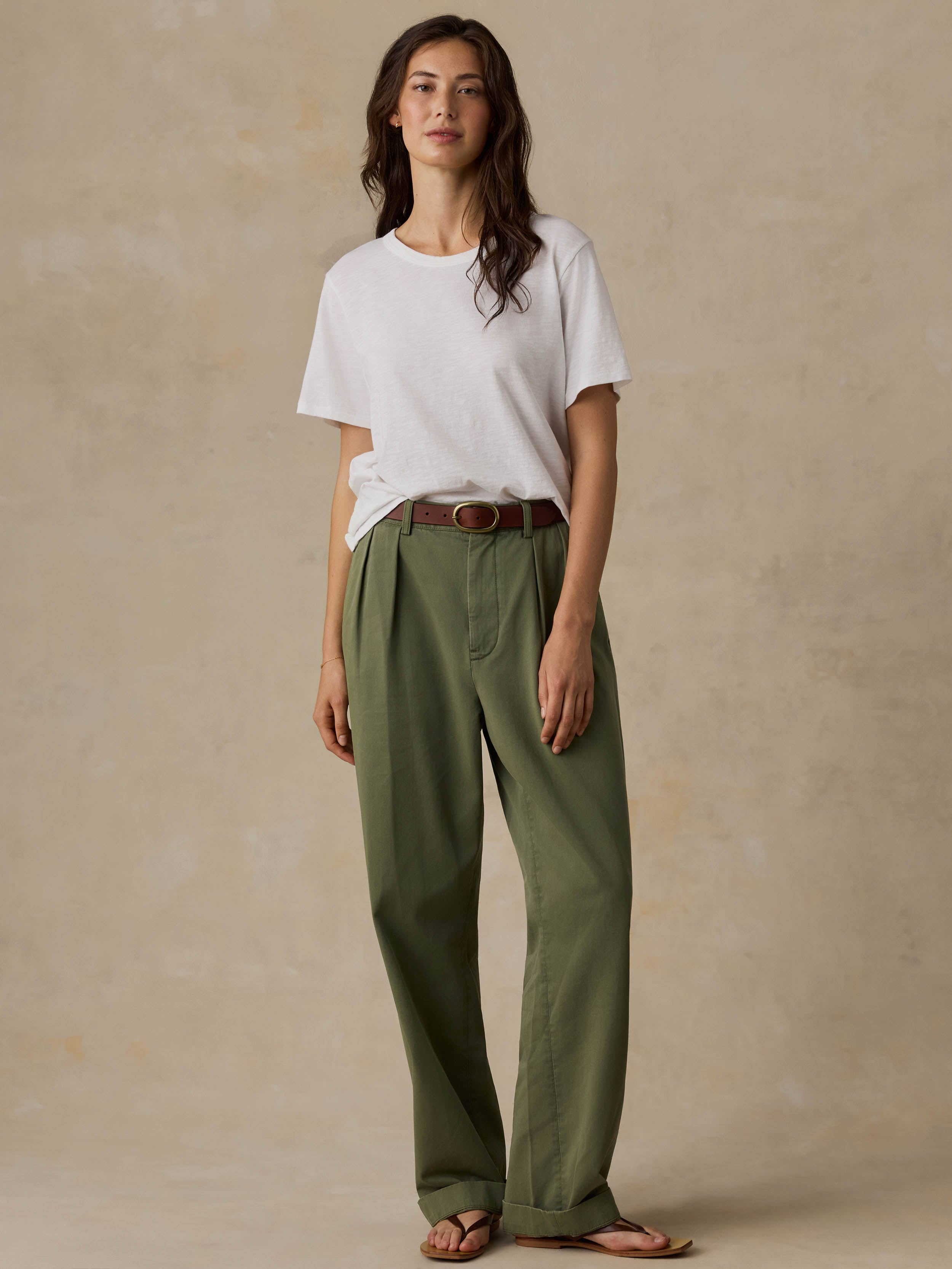 Woman wearing a white t-shirt and green pants against a beige background