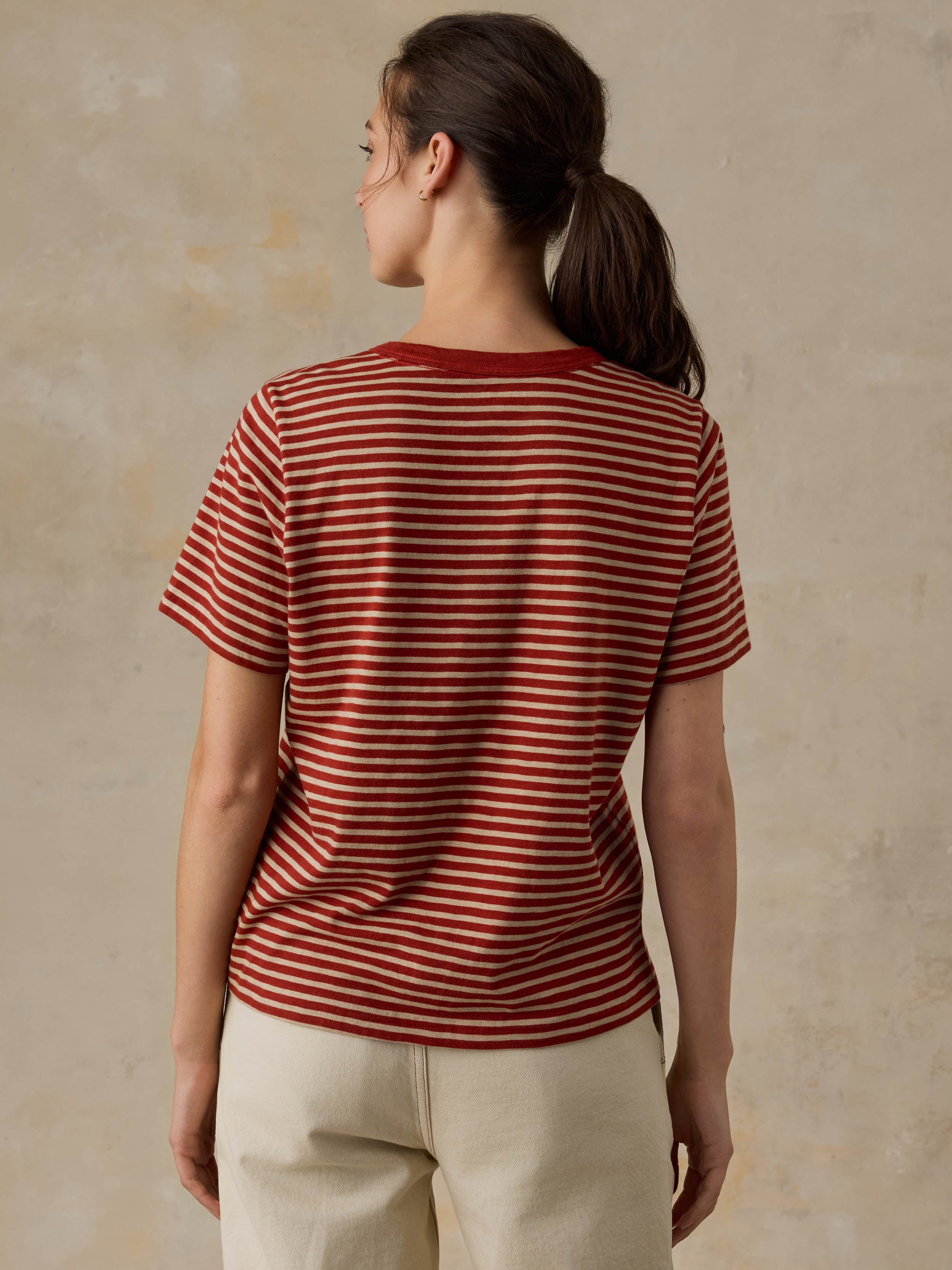 Woman wearing a red striped shirt and beige pants against a beige background