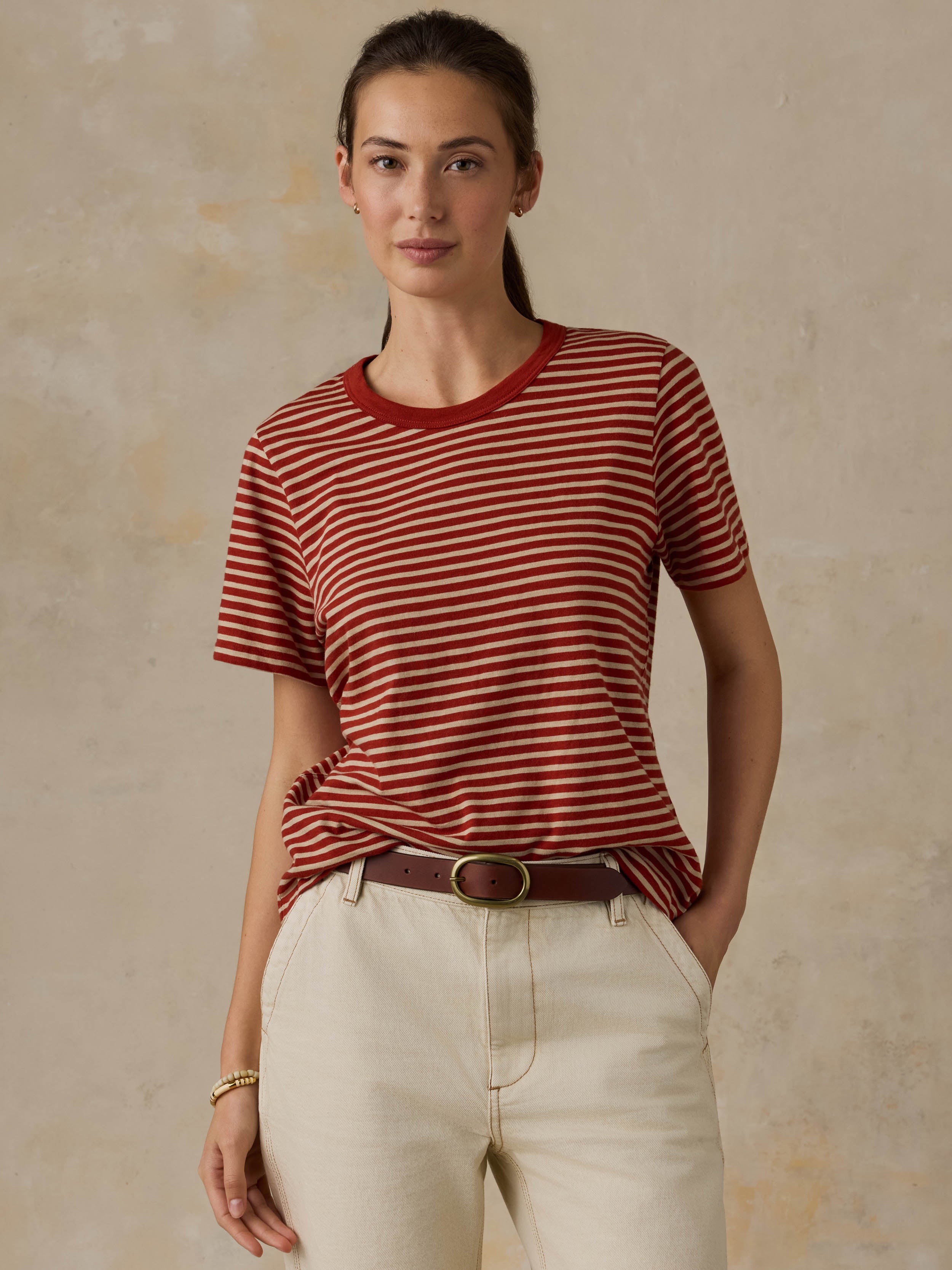 Woman wearing a red striped shirt and beige pants against a beige background