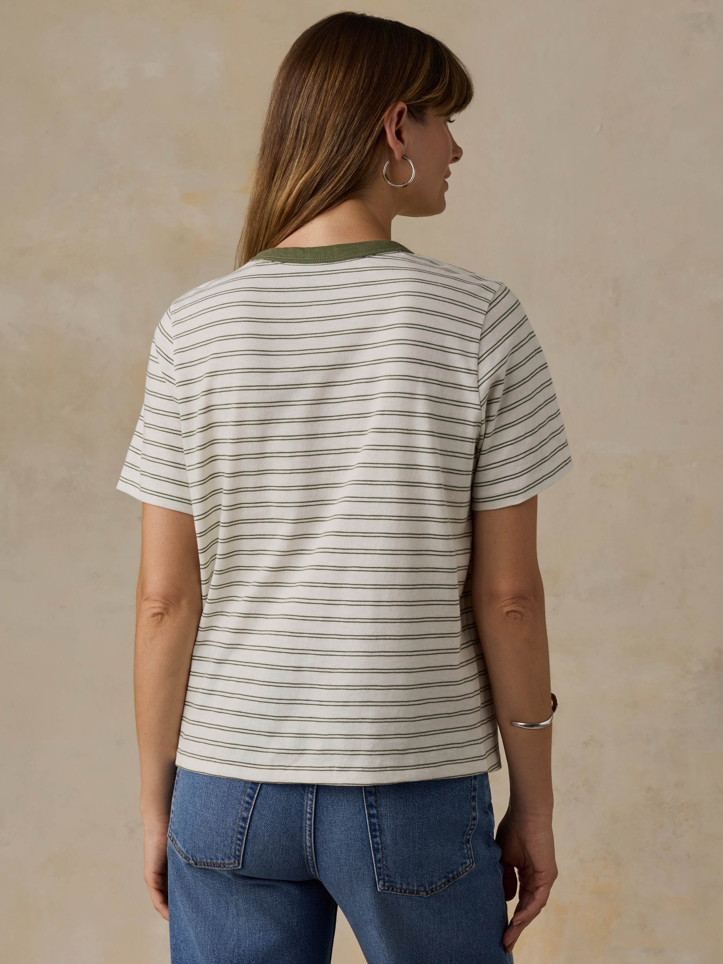 Woman wearing a green striped t-shirt and jeans against a beige background