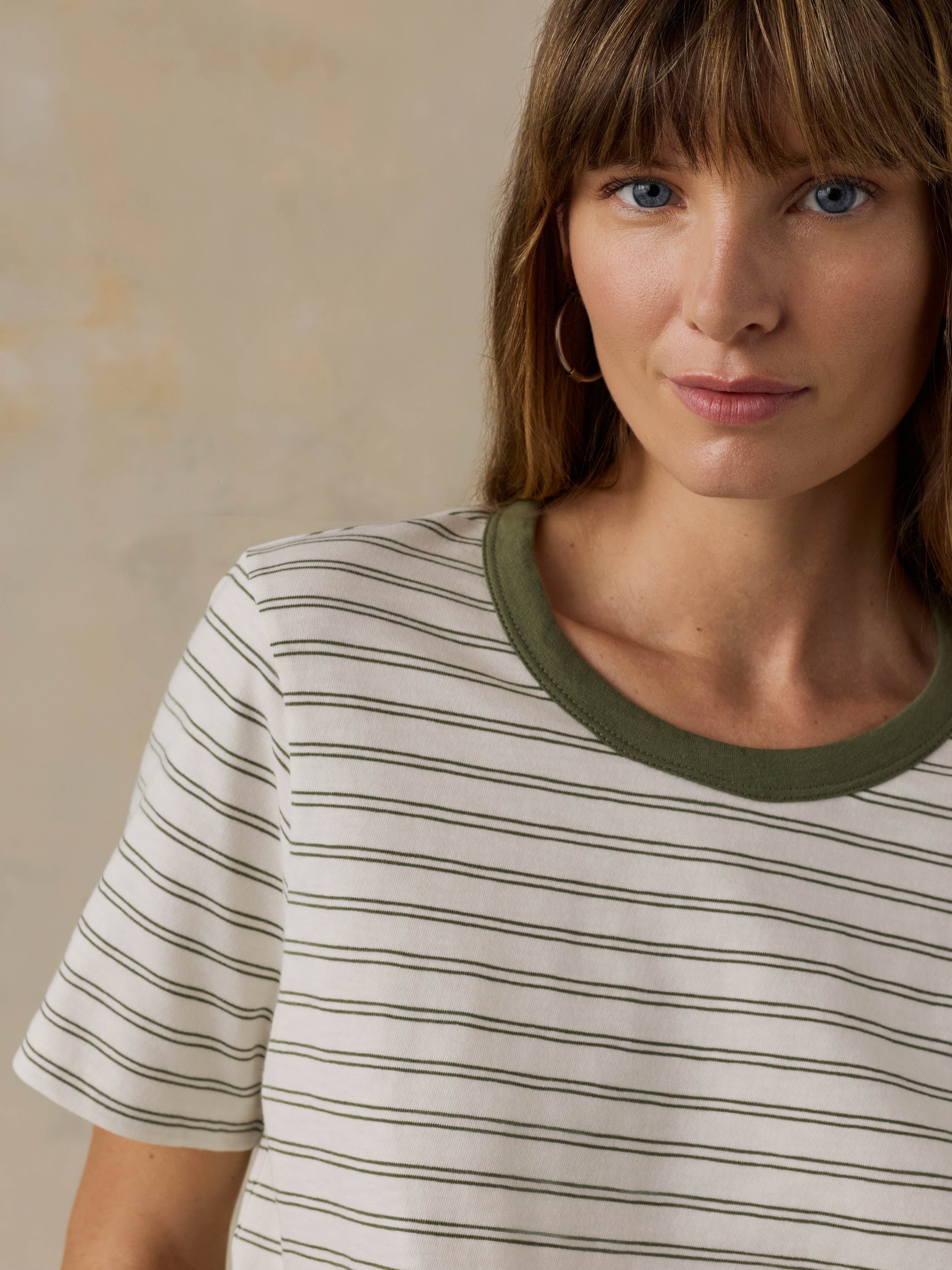 Woman wearing a green striped t-shirt against a beige background