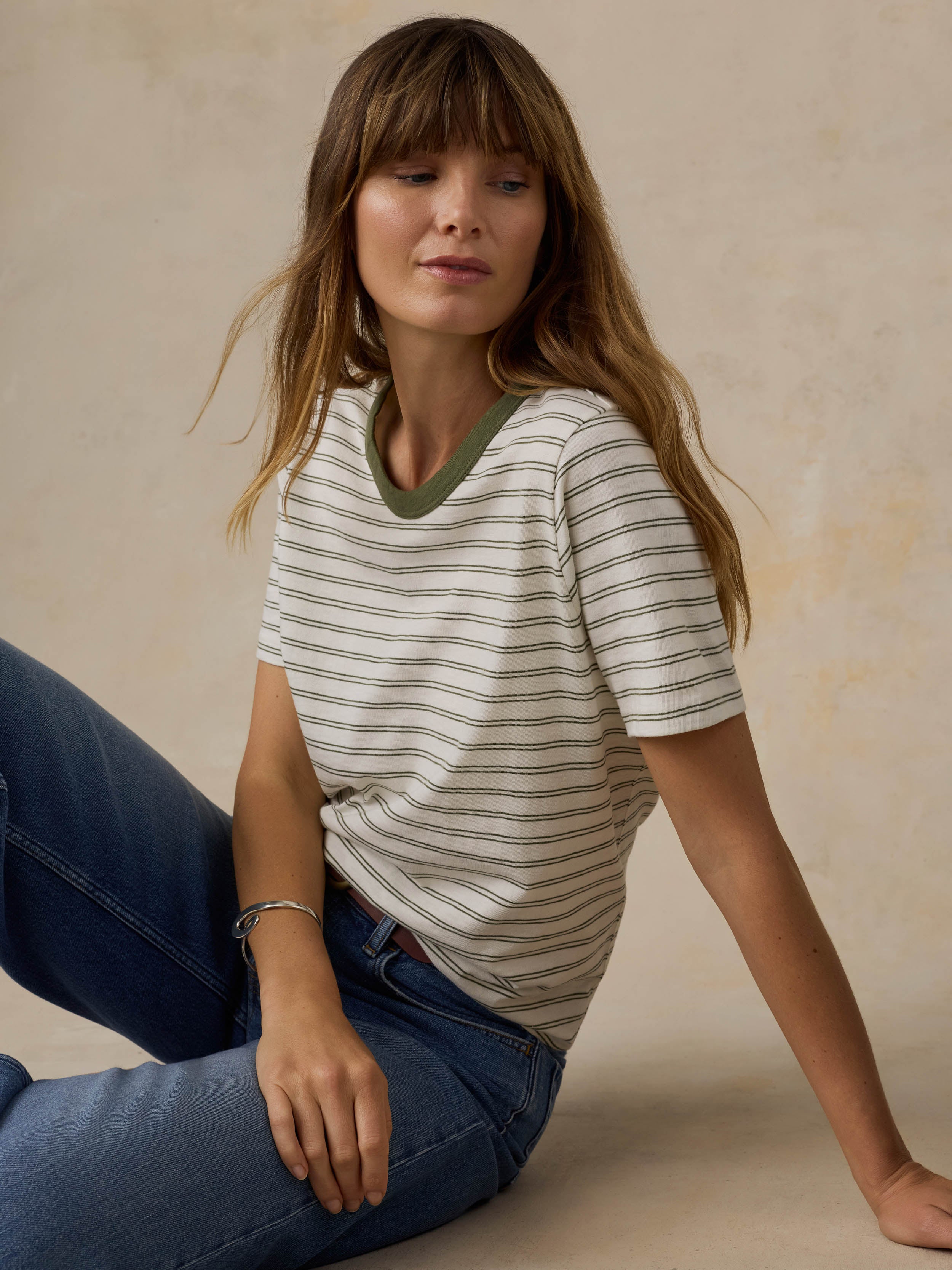 Woman wearing a green striped t-shirt and jeans against a beige background
