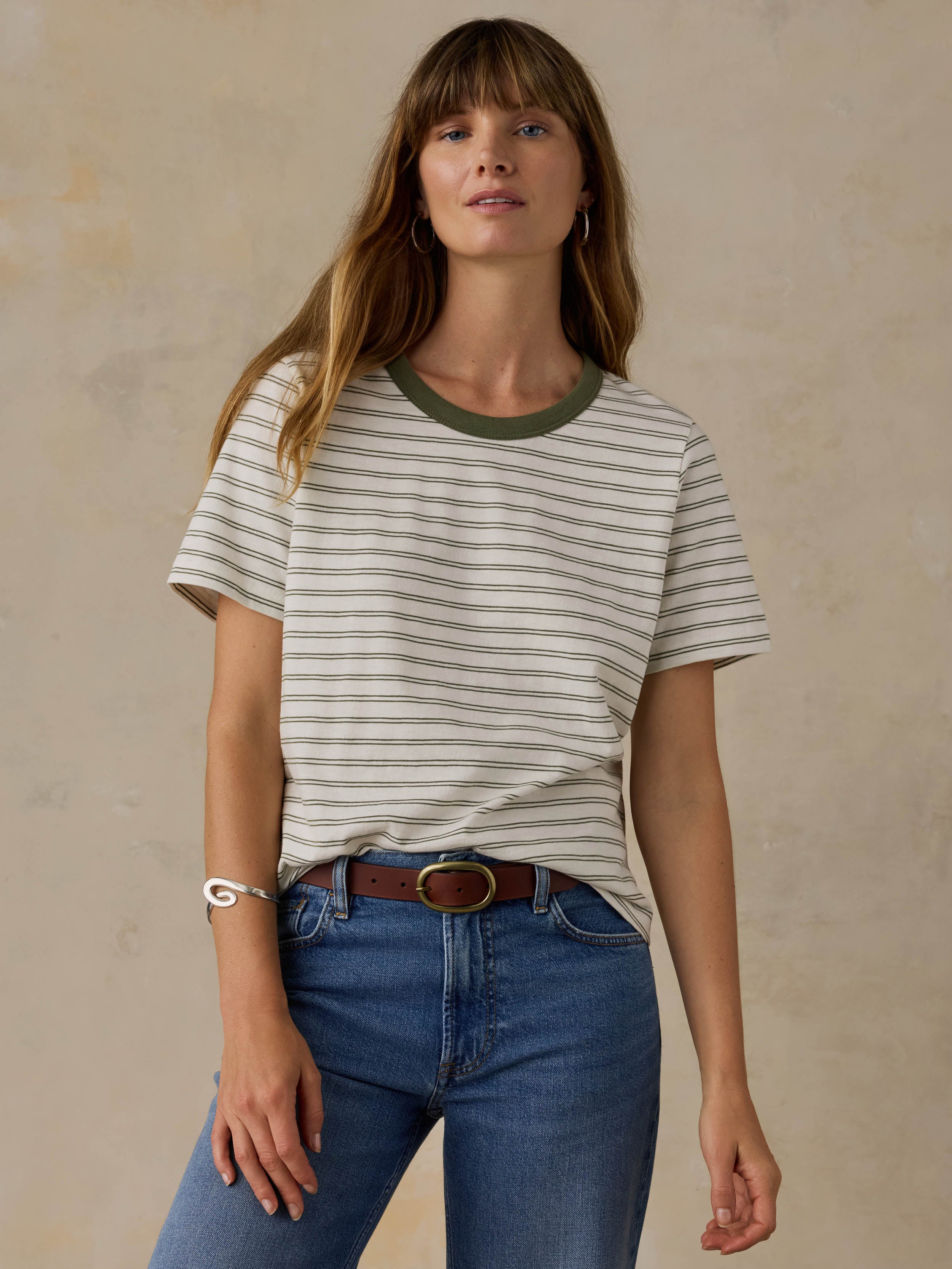 Woman wearing a green striped t-shirt and jeans against a beige background