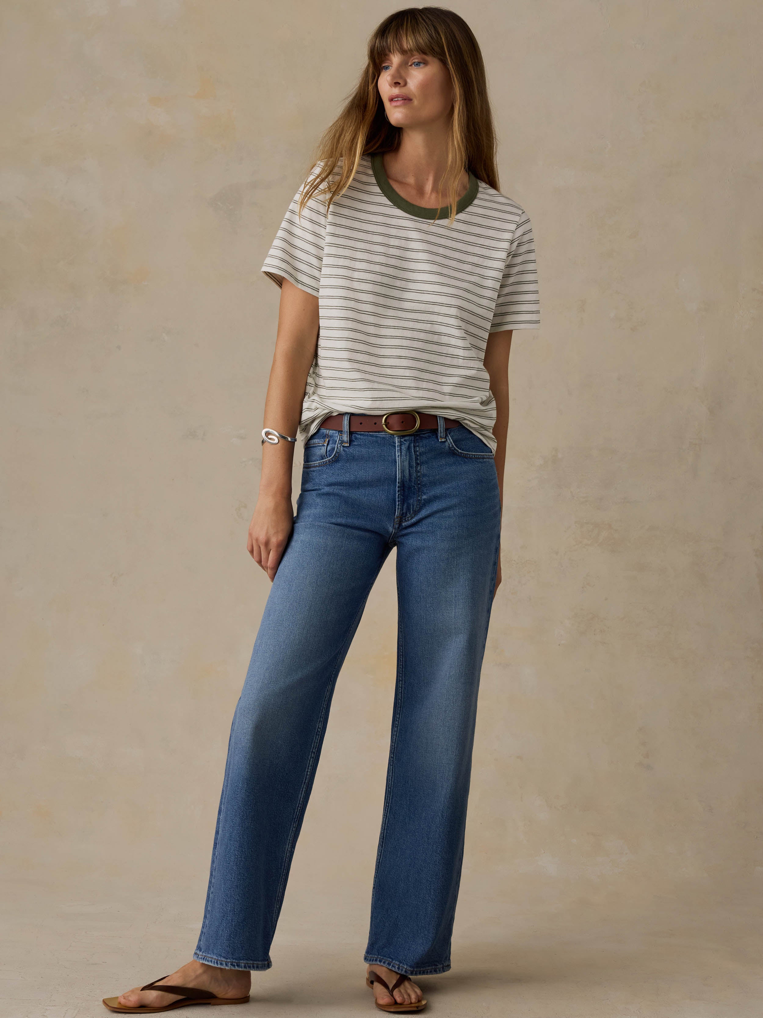 Woman wearing a green striped t-shirt and jeans against a beige background