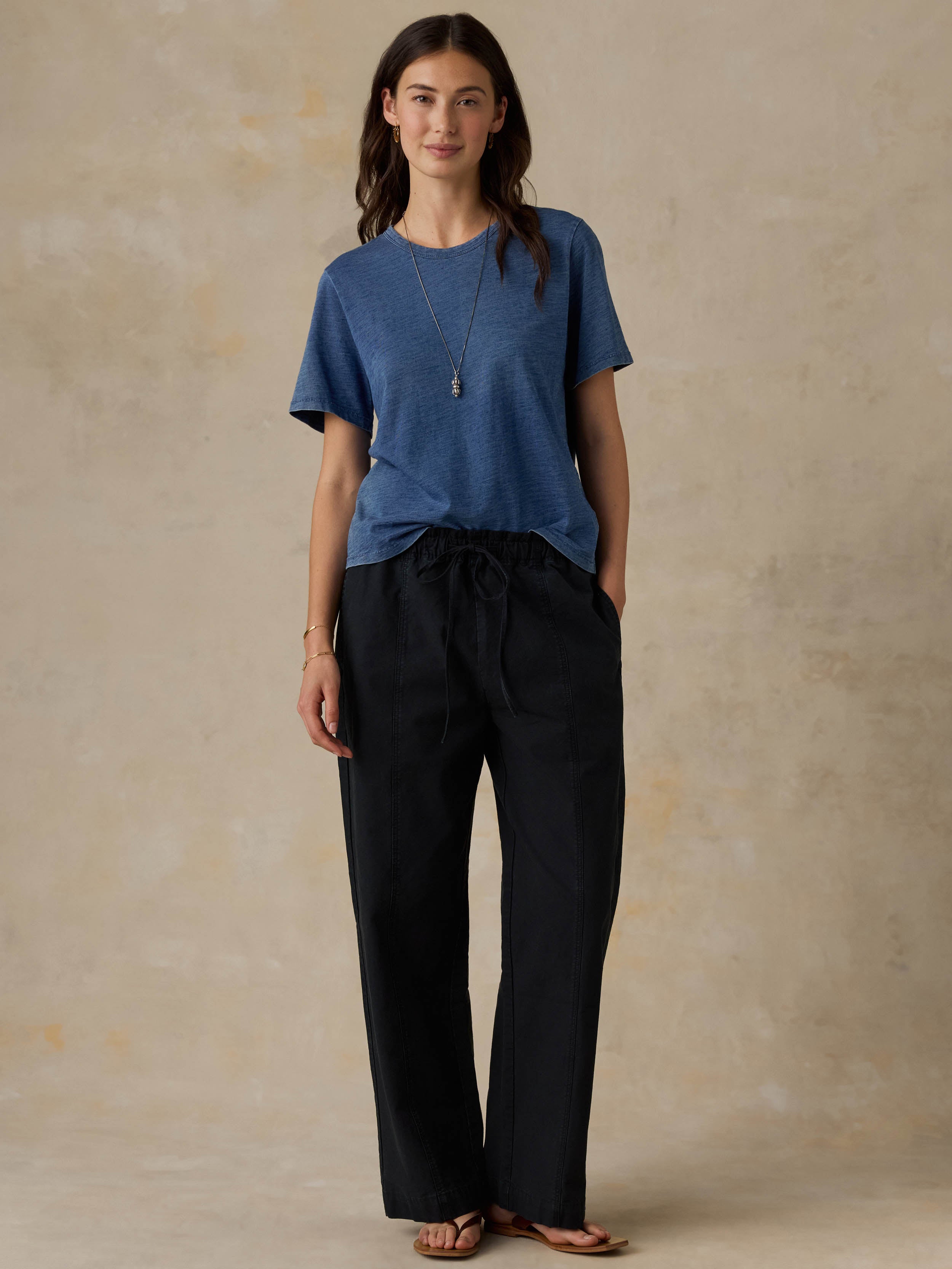 Woman wearing a blue t-shirt and black pants against a beige background