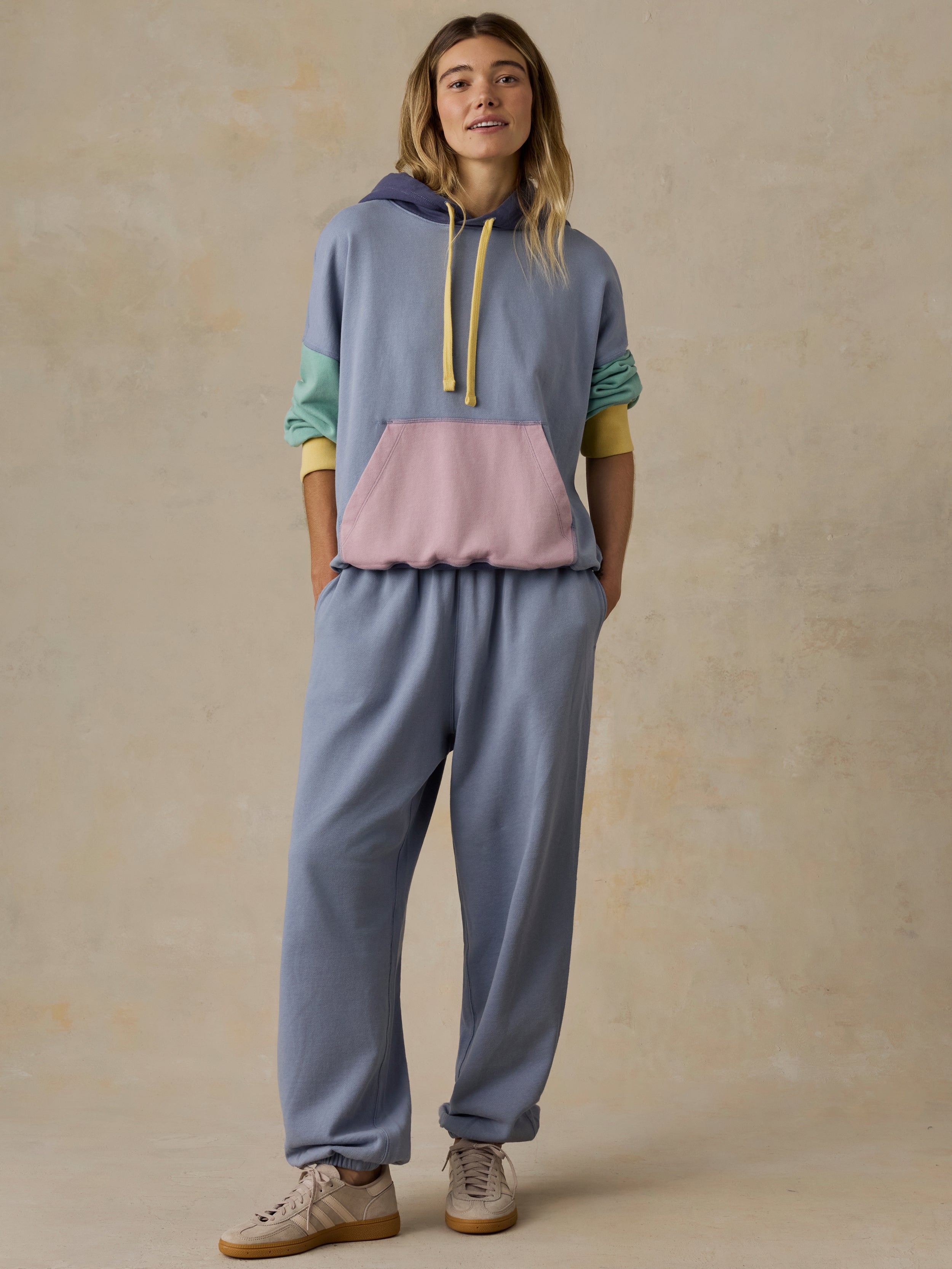 Woman wearing a colorblocked hoodie and purple sweatpants against a beige background