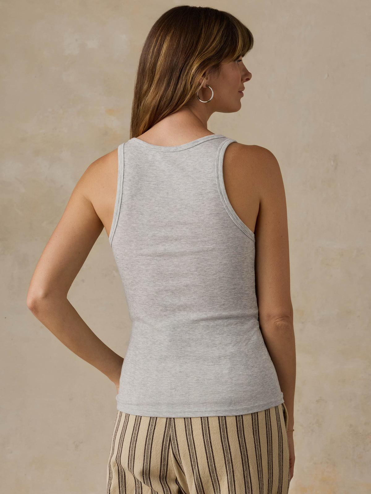 Woman wearing a grey tank top and striped pants against a beige background, image 4 of 5