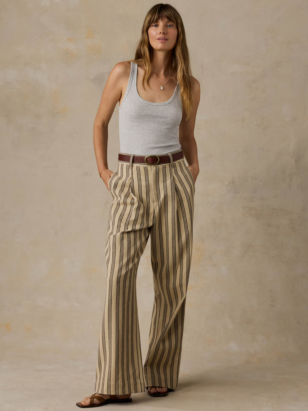 Woman wearing a grey tank top and striped pants against a beige background, image 5 of 5