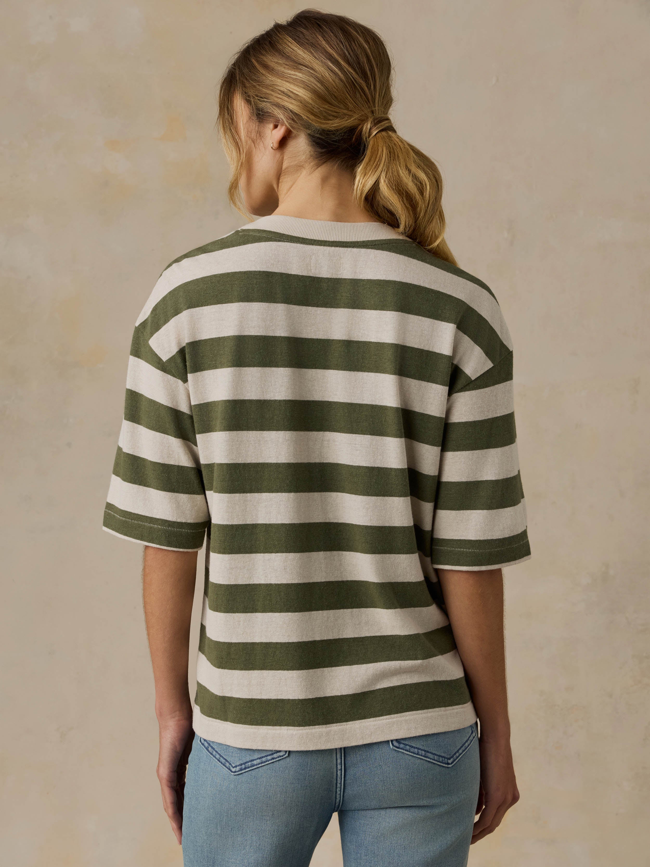Woman wearing a green and white striped shirt with blue jeans against a beige background