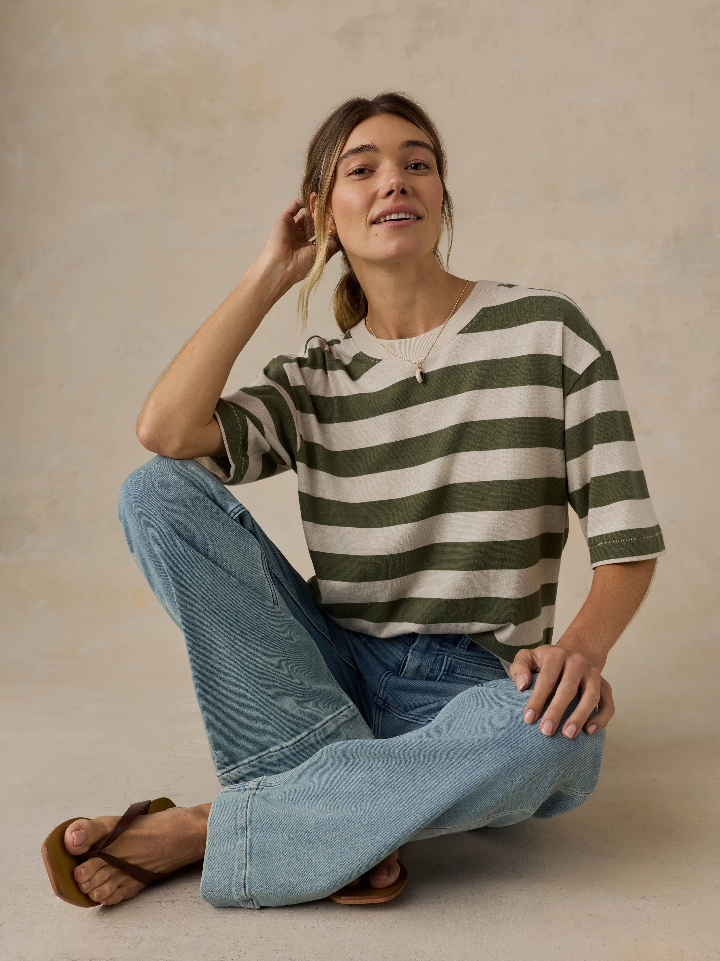 Woman wearing a green and white striped shirt with blue jeans against a beige background