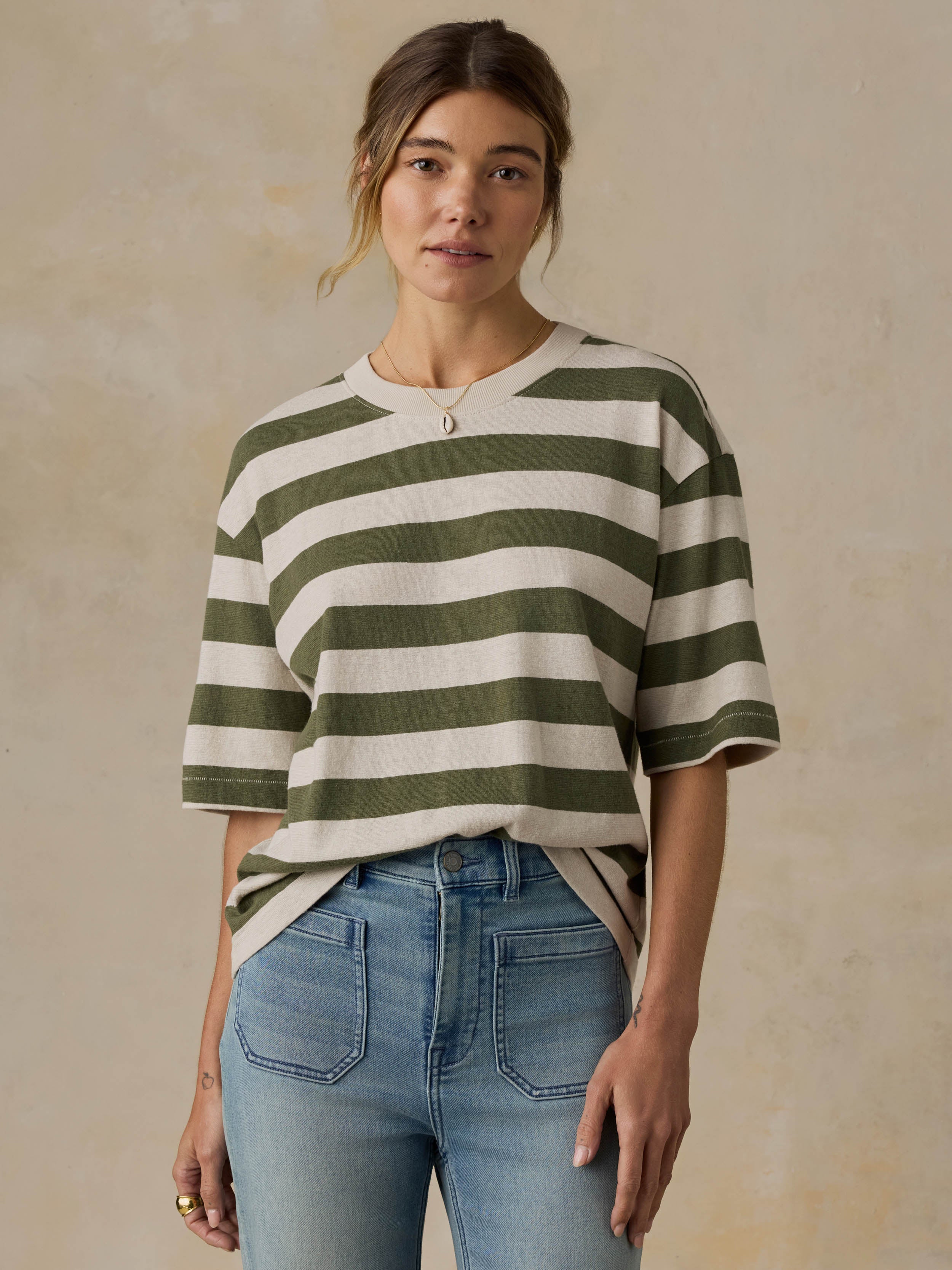 Woman wearing a green and white striped shirt with blue jeans against a beige background