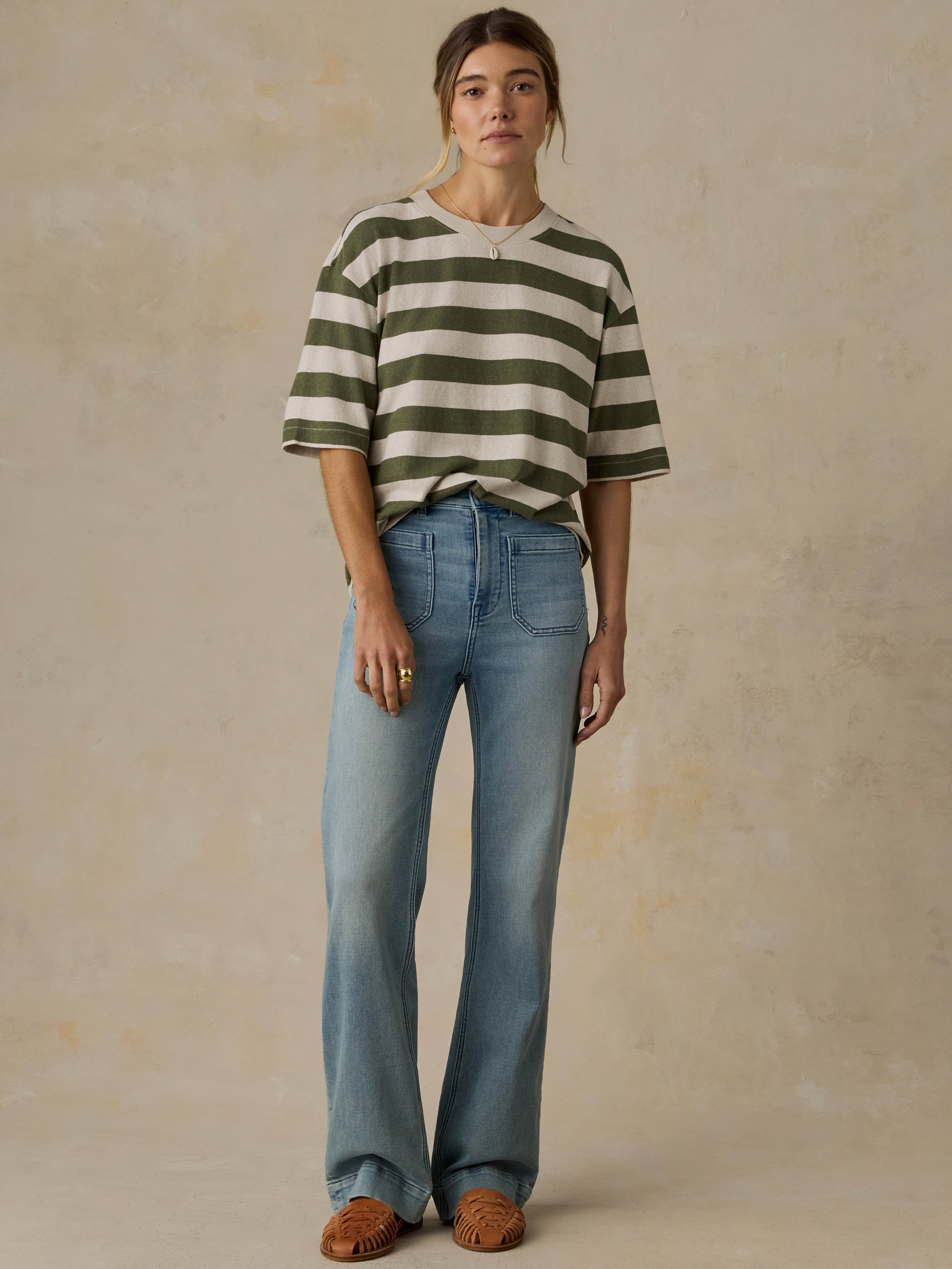 Woman wearing a green and white striped shirt with blue jeans against a beige background