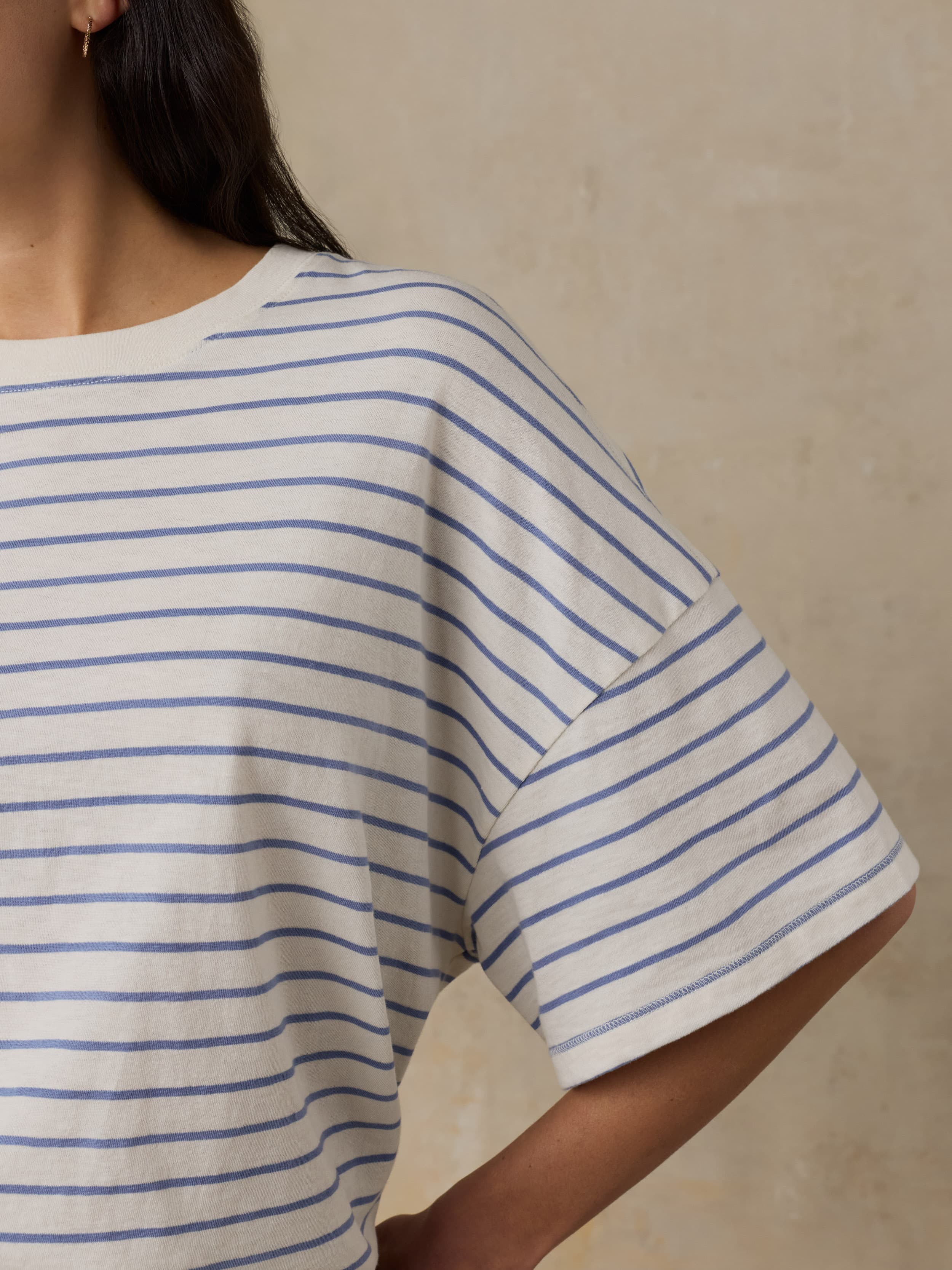 Woman wearing a white t-shirt with blue stripes against a beige background