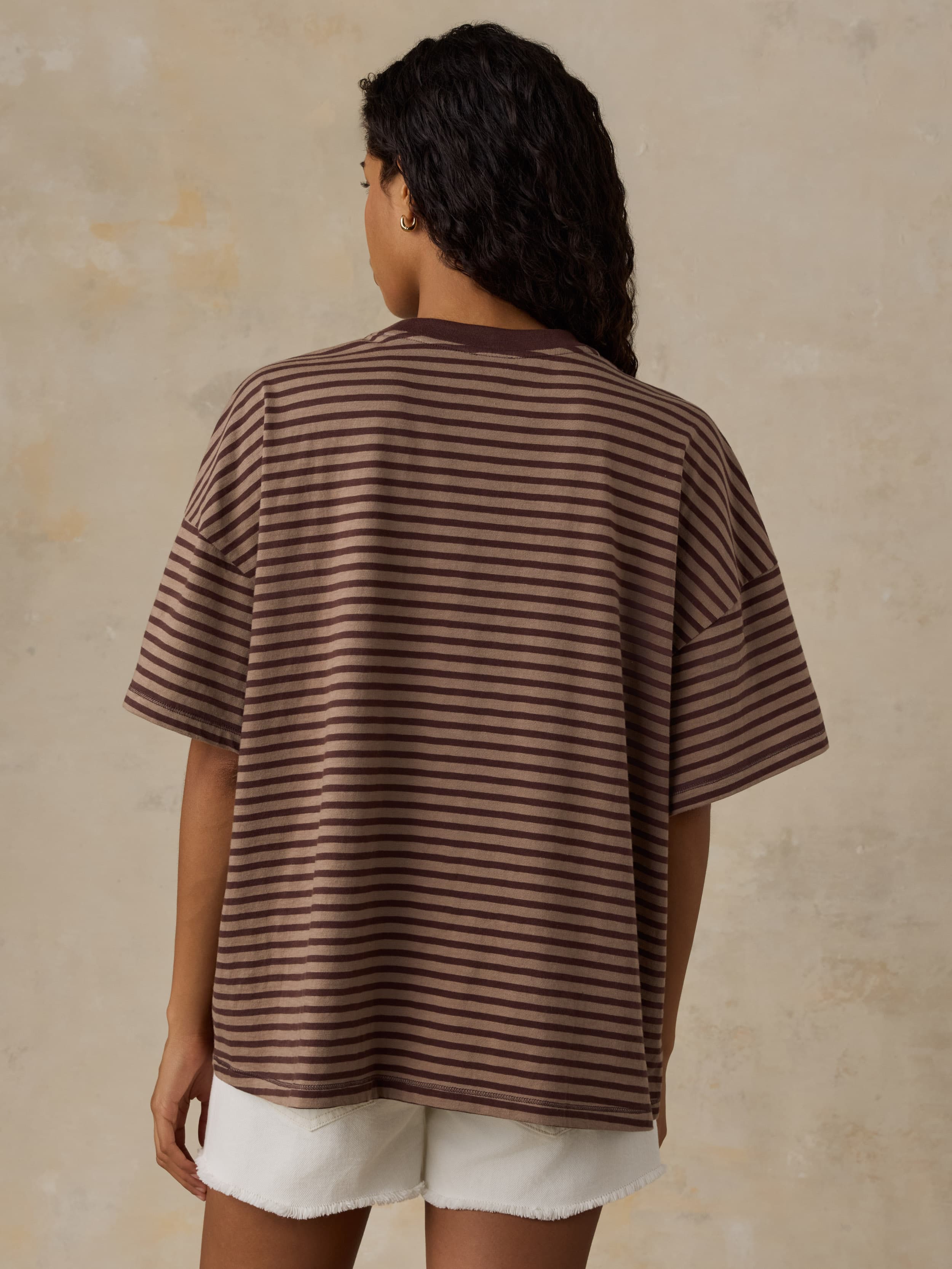 Woman wearing a brown striped shirt and white shorts against a beige background
