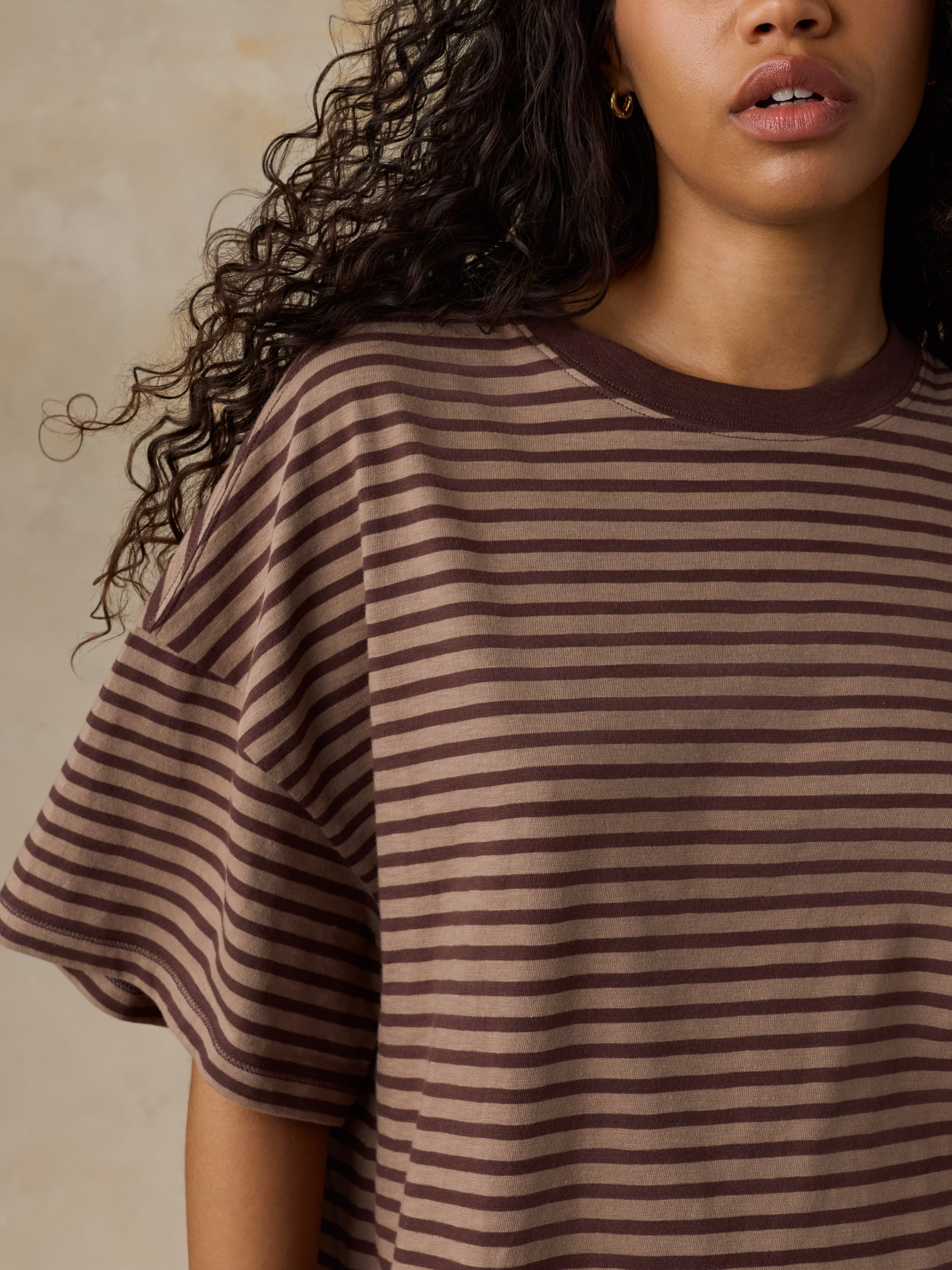 Woman wearing a brown and beige striped shirt against a neutral background