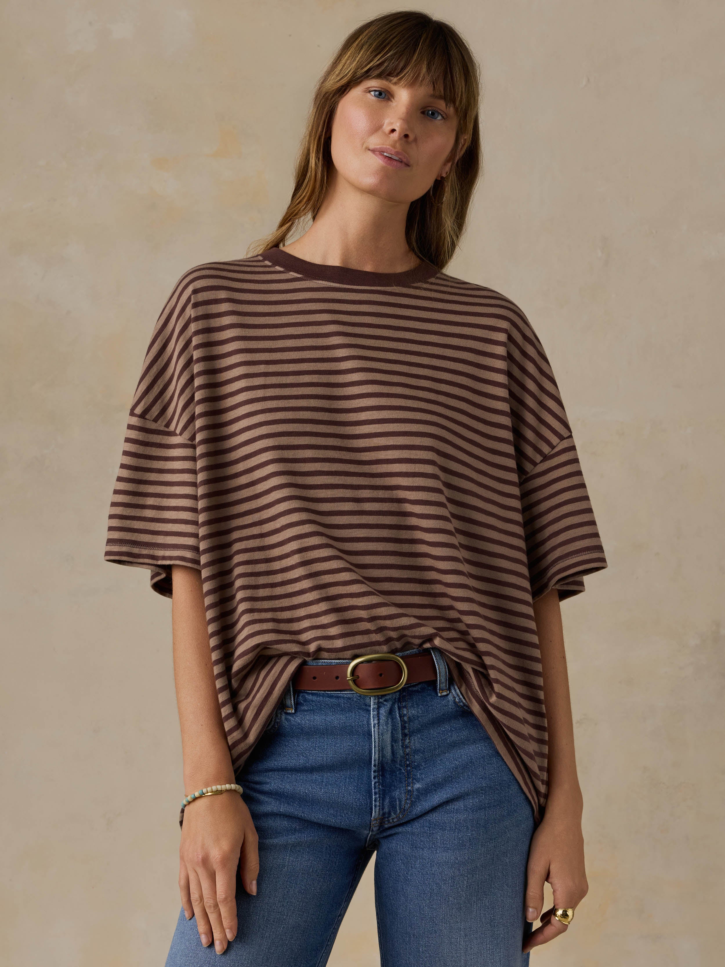 Woman wearing a brown striped shirt and blue jeans against a beige background