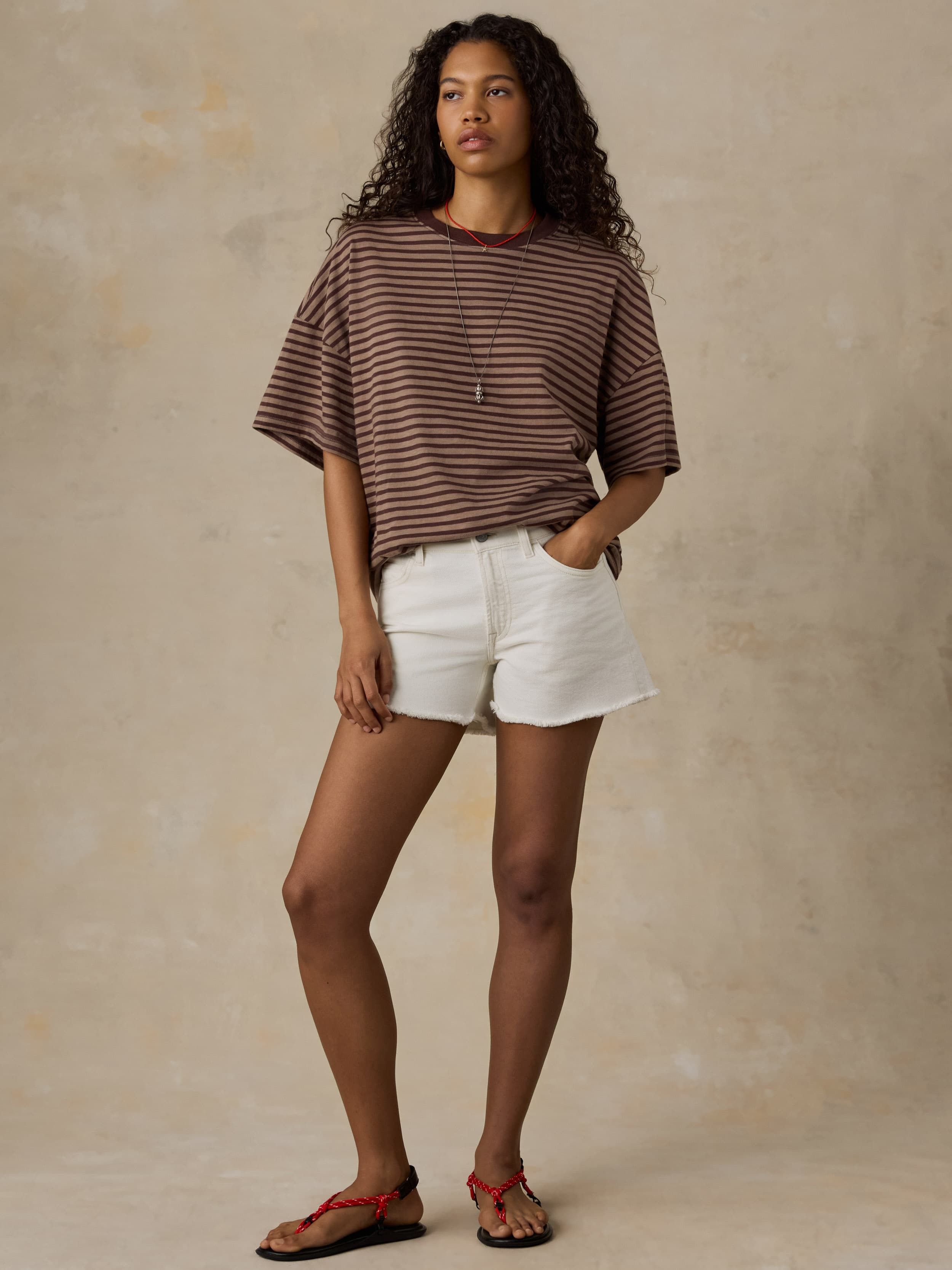 Woman wearing a brown striped shirt and white shorts against a beige background