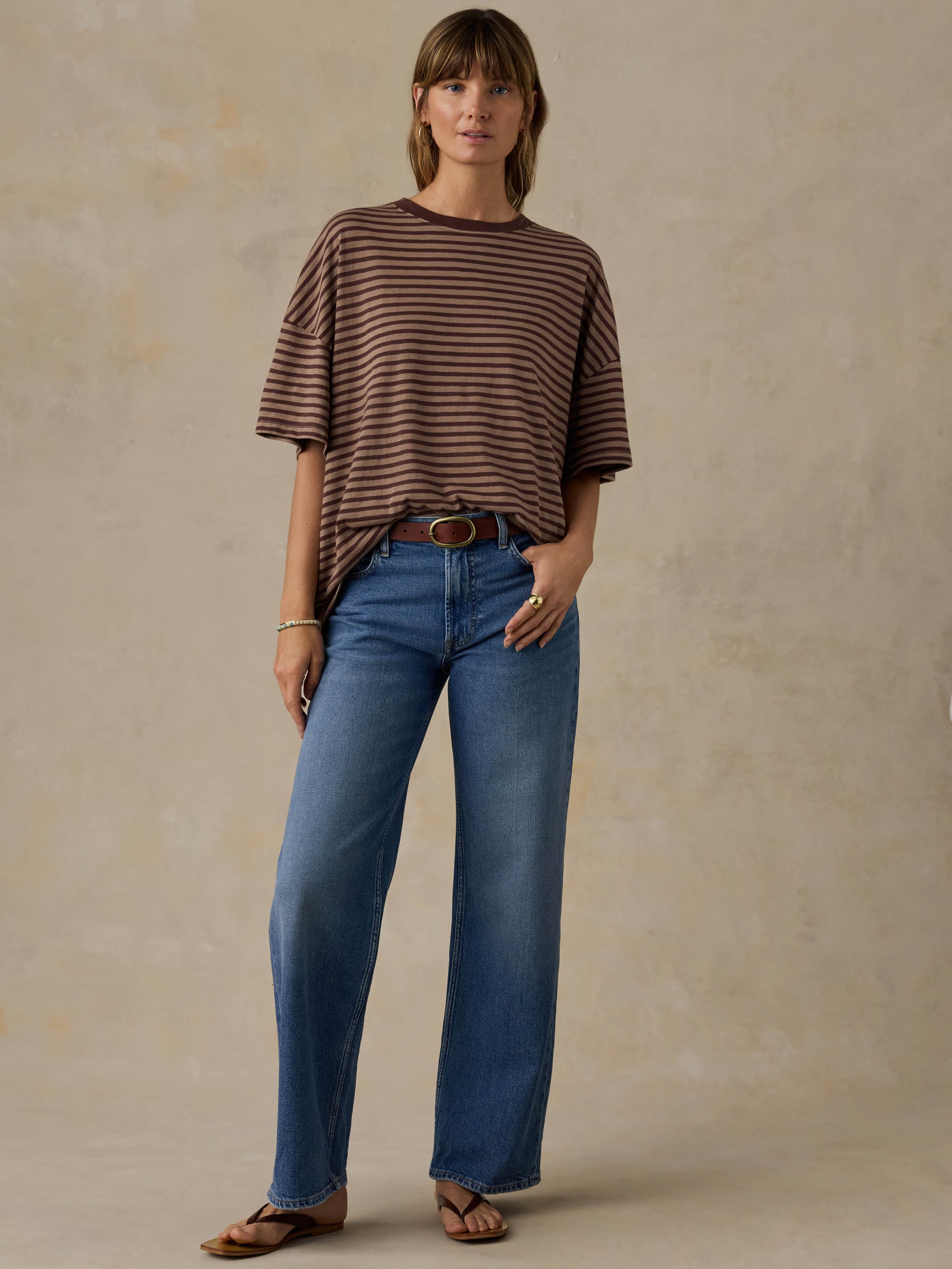 Woman wearing a brown striped shirt and blue jeans against a beige background