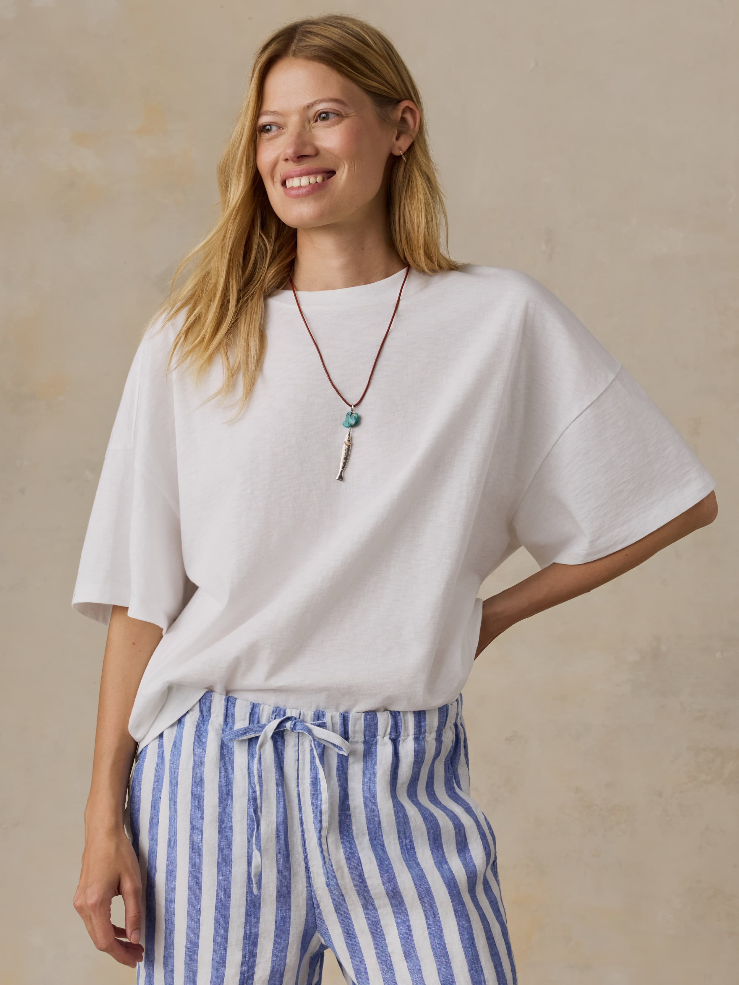 Woman wearing a white oversized t-shirt and blue striped pants against a beige background