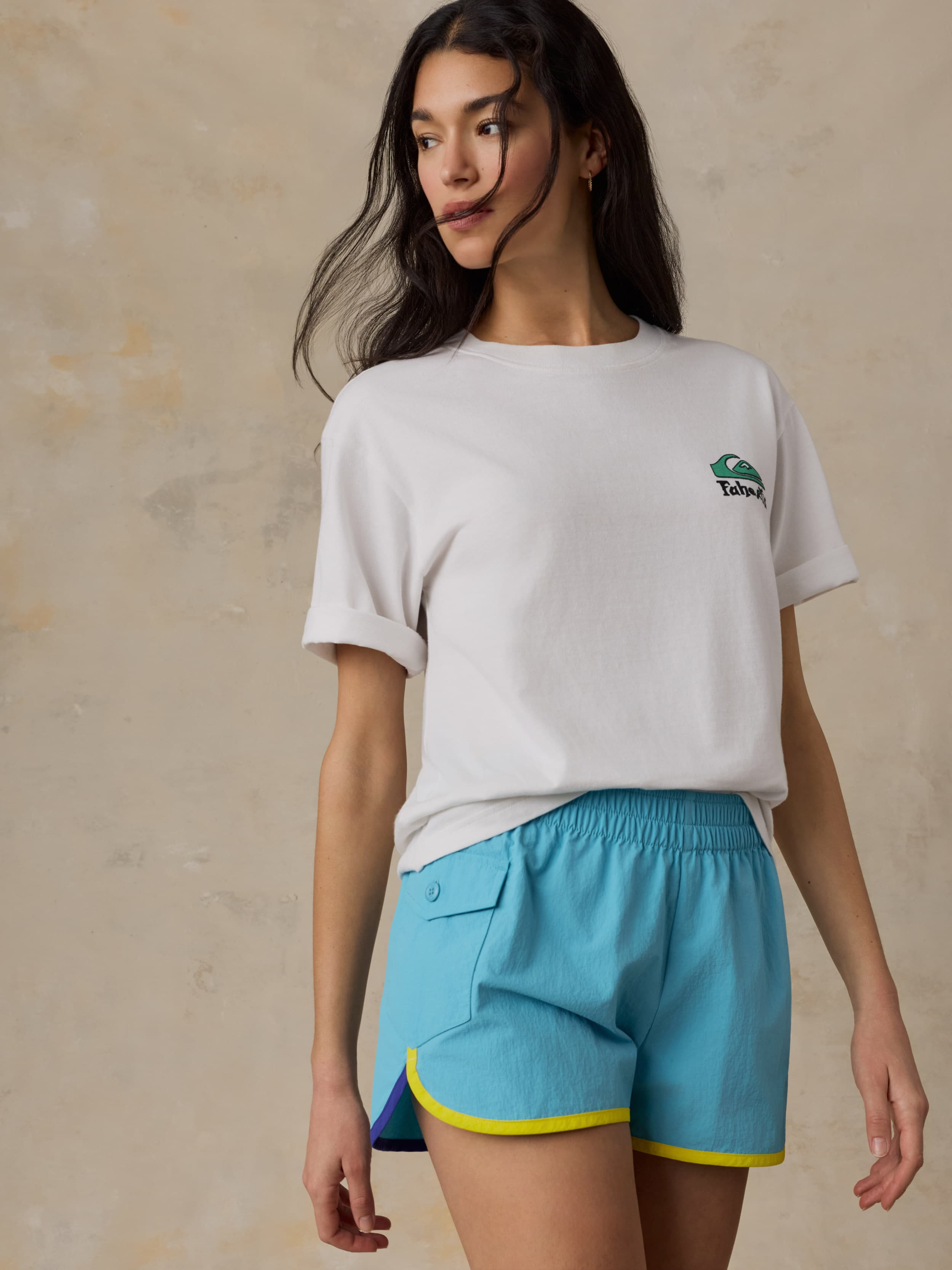 Woman wearing a white t-shirt with a logo and blue shorts on a beige background