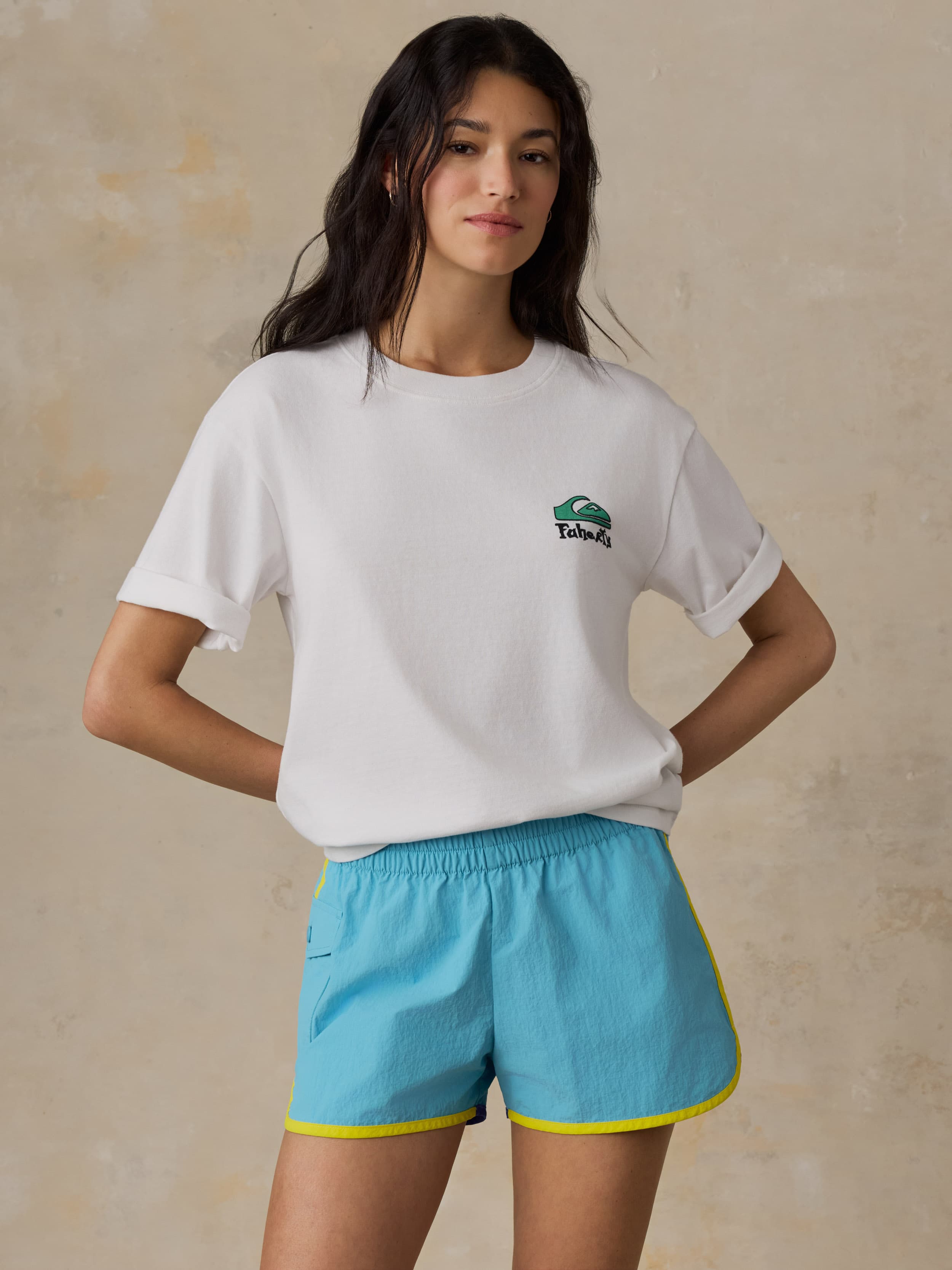 Woman wearing a white t-shirt with a logo and blue shorts on a beige background
